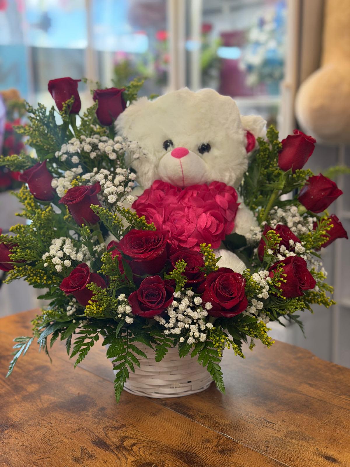 White teddy bear surrounded by red roses in a basket