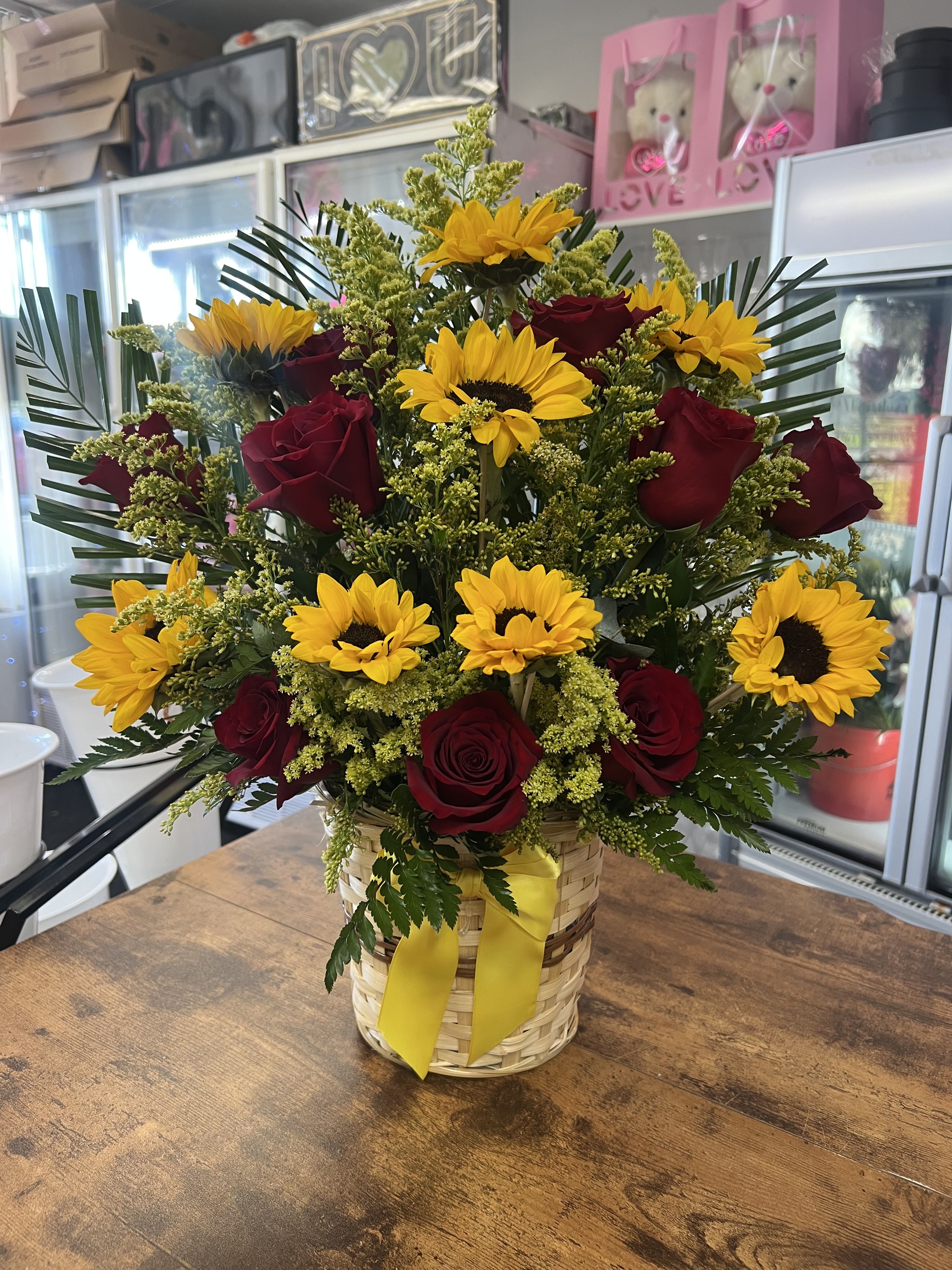Basket arrangement of red roses and yellow sunflowers with a yellow ribbon