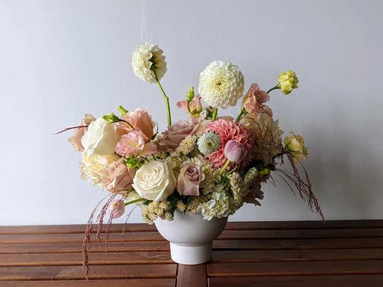 Lush Spring Garden Collection - Beautiful, modern and unforgettable floral artistry! This is our largest arrangement from our Spring Garden Collection and is the most impressive. An abundant, garden-style arrangement designed with lush layers of soft spring blooms in romantic shades of peach, blush, buttery tones, and pops of lavender. With a wider, more expansive shape, this design is filled with movement and texture, creating the feeling of a flourishing spring garden in full bloom.  Featuring premium seasonal flowers like ranunculus, garden roses, peonies, and delicate accents, each arrangement is thoughtfully styled in a ceramic vessel for a natural, effortless look.  Perfect for making a statement, celebrating meaningful moments, or filling a space with the beauty and softness of spring.  *Flowers and vases are natural and artisan products, and no two arrangements are exactly alike. While your arrangement may differ slightly from the photo, it will be designed with the same style and color palette of your choice. Occasionally, substitutions of vases may be necessary due to market availability, but we will always substitute with a vase of equal or greater value.