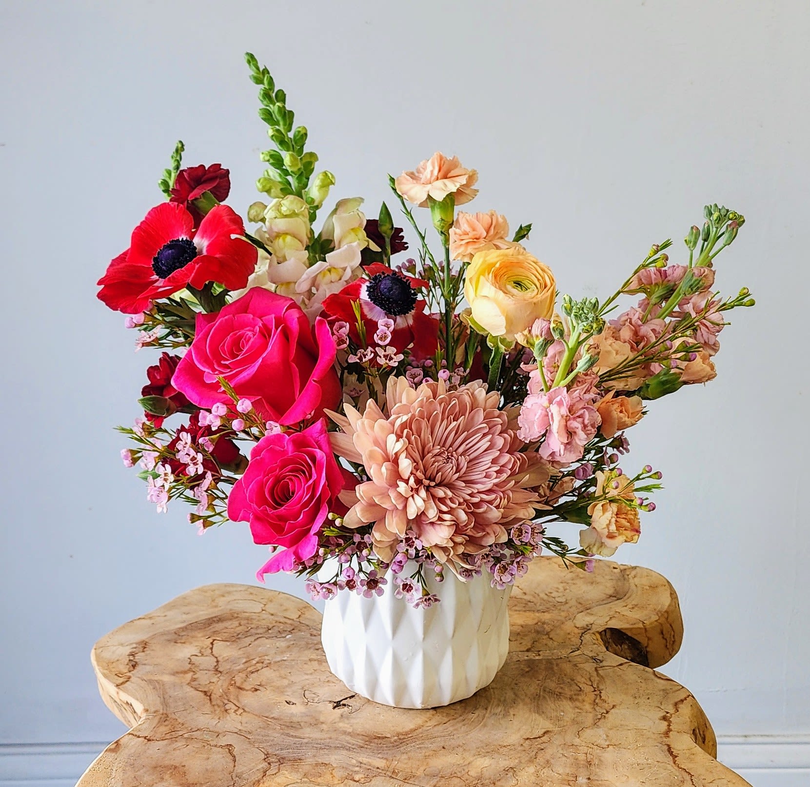 Mixed bouquet of pink, peach, and red flowers in a white vase
