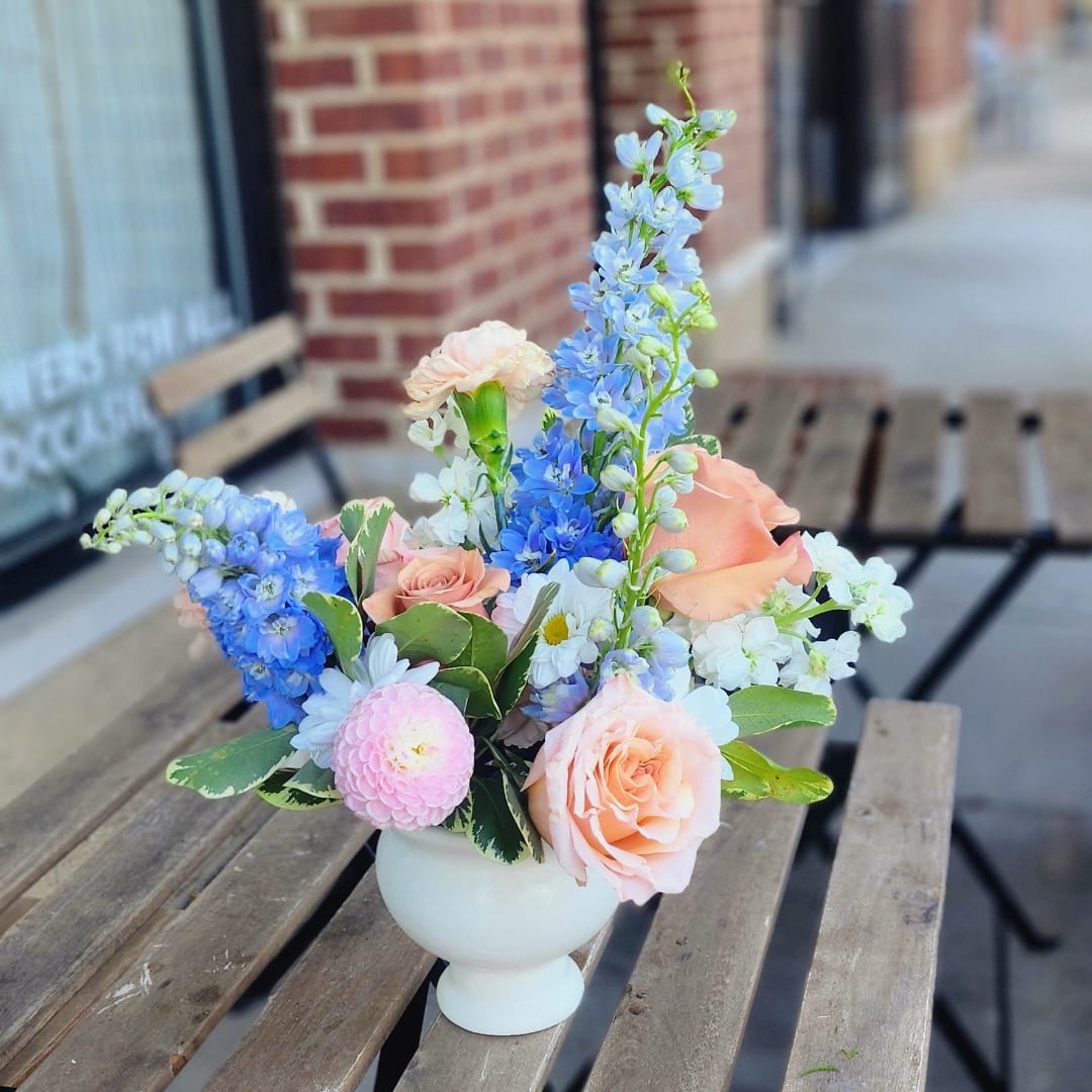Pastel flower arrangement in a white vase with roses and blue delphinium
