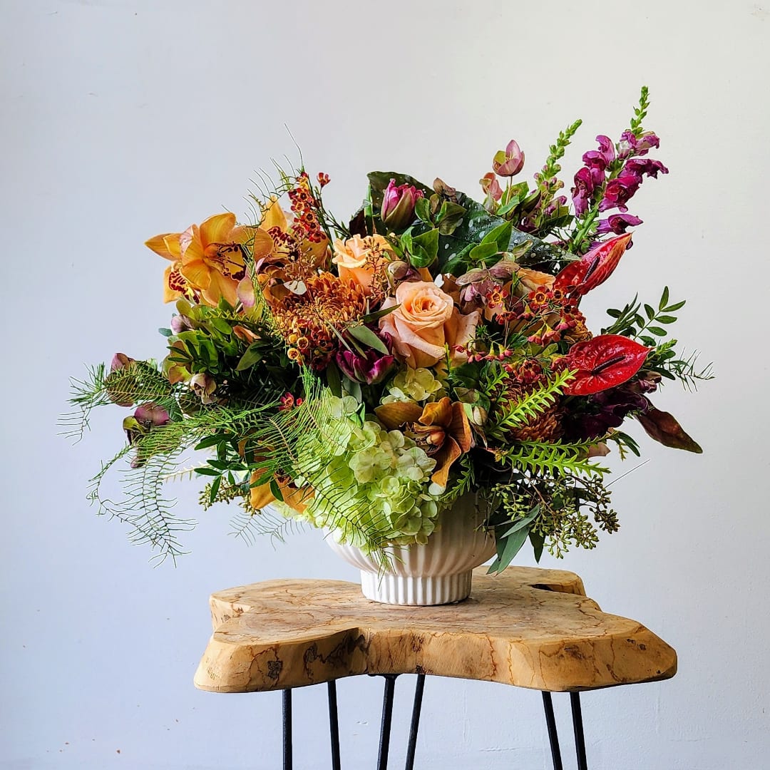 Mixed floral arrangement in a white vase with orange, pink, and red blooms