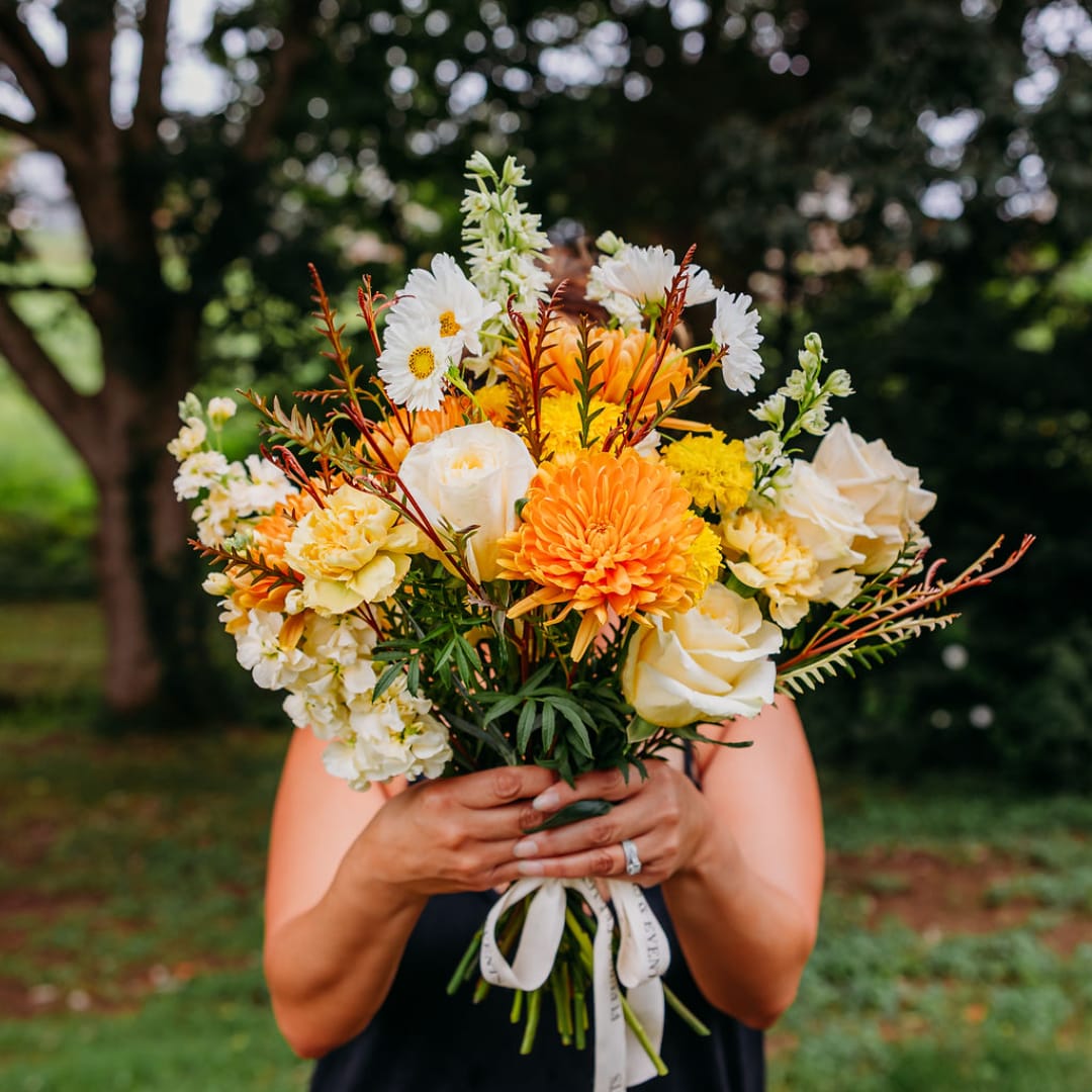 Woman holding a bouquet of orange, white, and yellow flowers