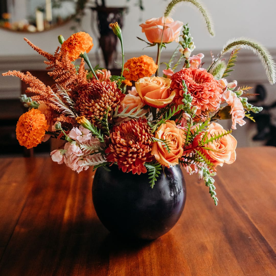 Orange and peach flowers arranged in a black vase on a wooden table
