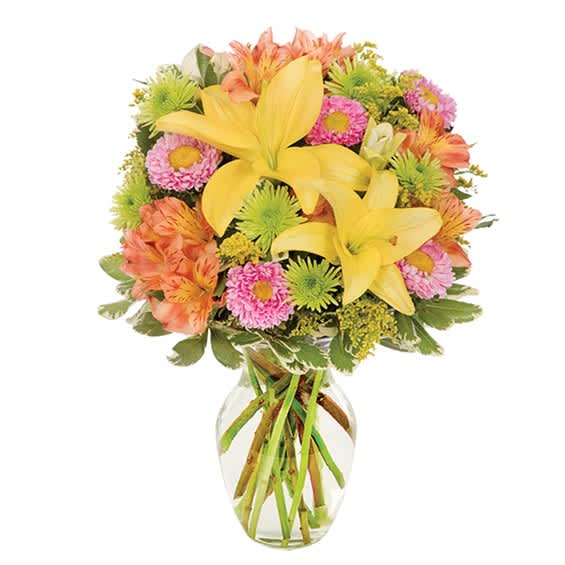 Mixed bouquet of yellow lilies, pink daisies, and orange flowers in a clear glass vase