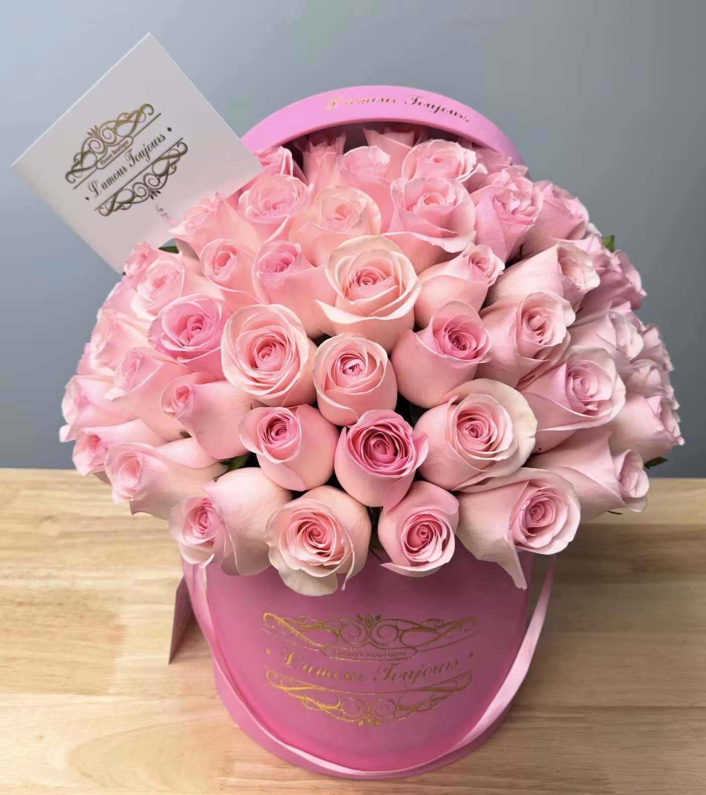 Pink roses arranged in a round hatbox with a card tucked in back