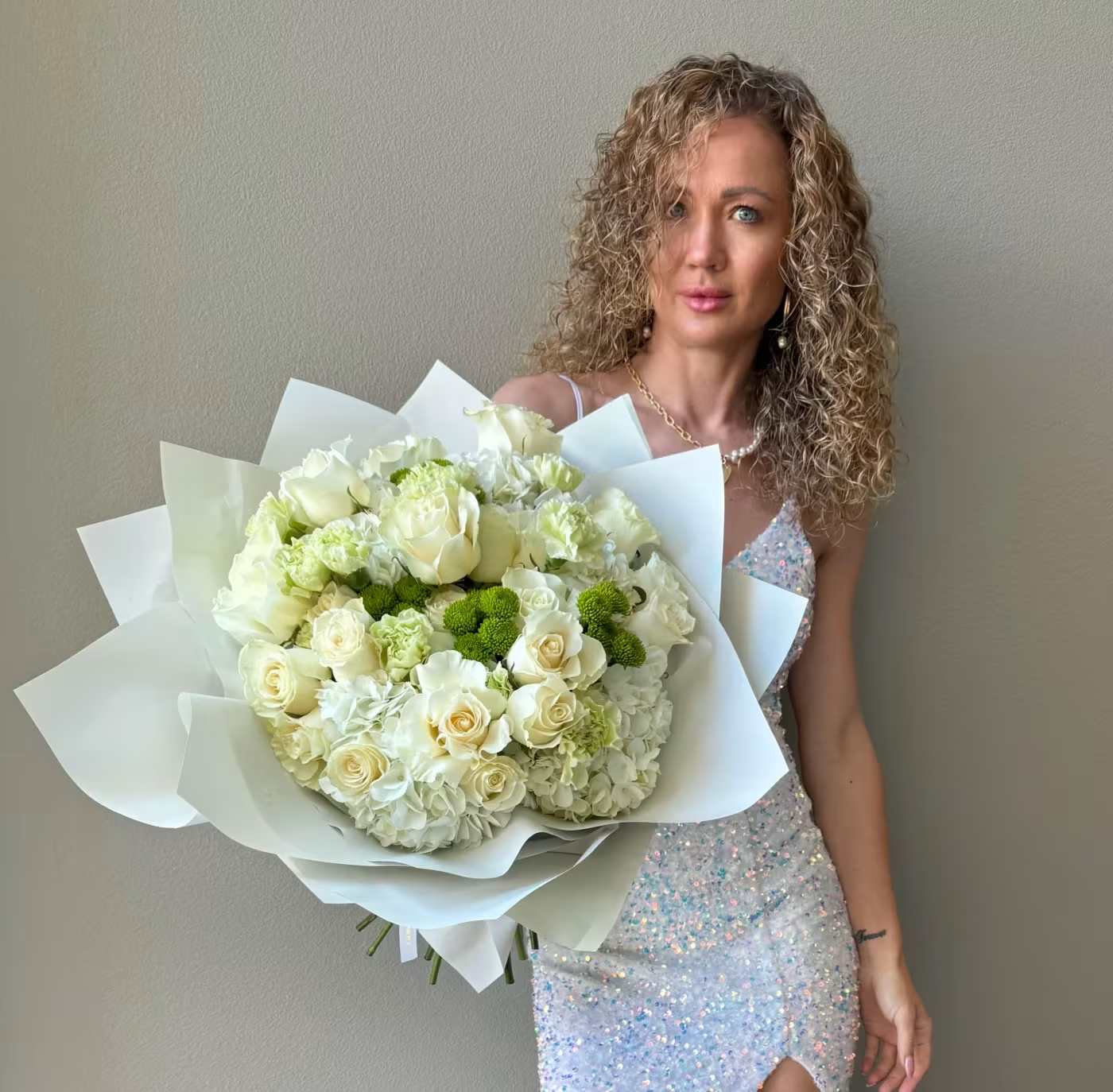 Woman holding a large bouquet of white roses and hydrangeas wrapped in white paper.