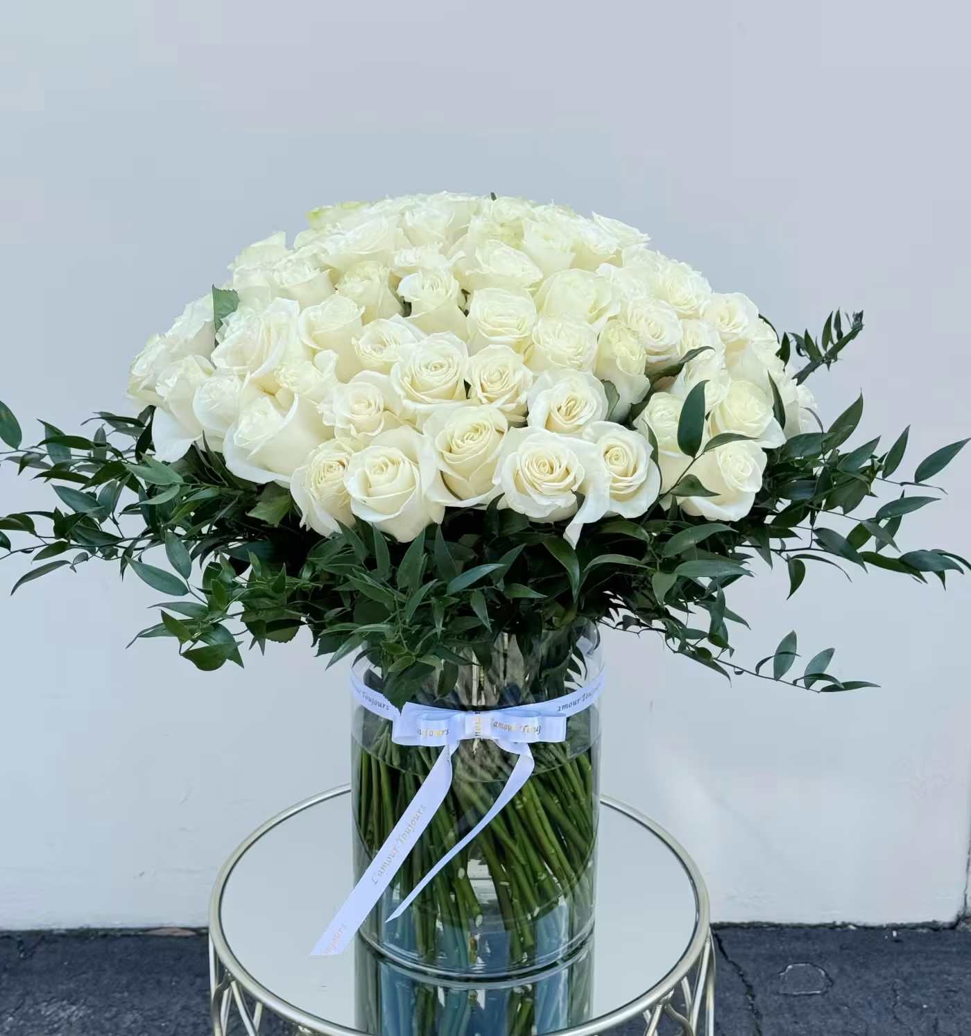 Large bouquet of white roses in a clear glass vase with a ribbon