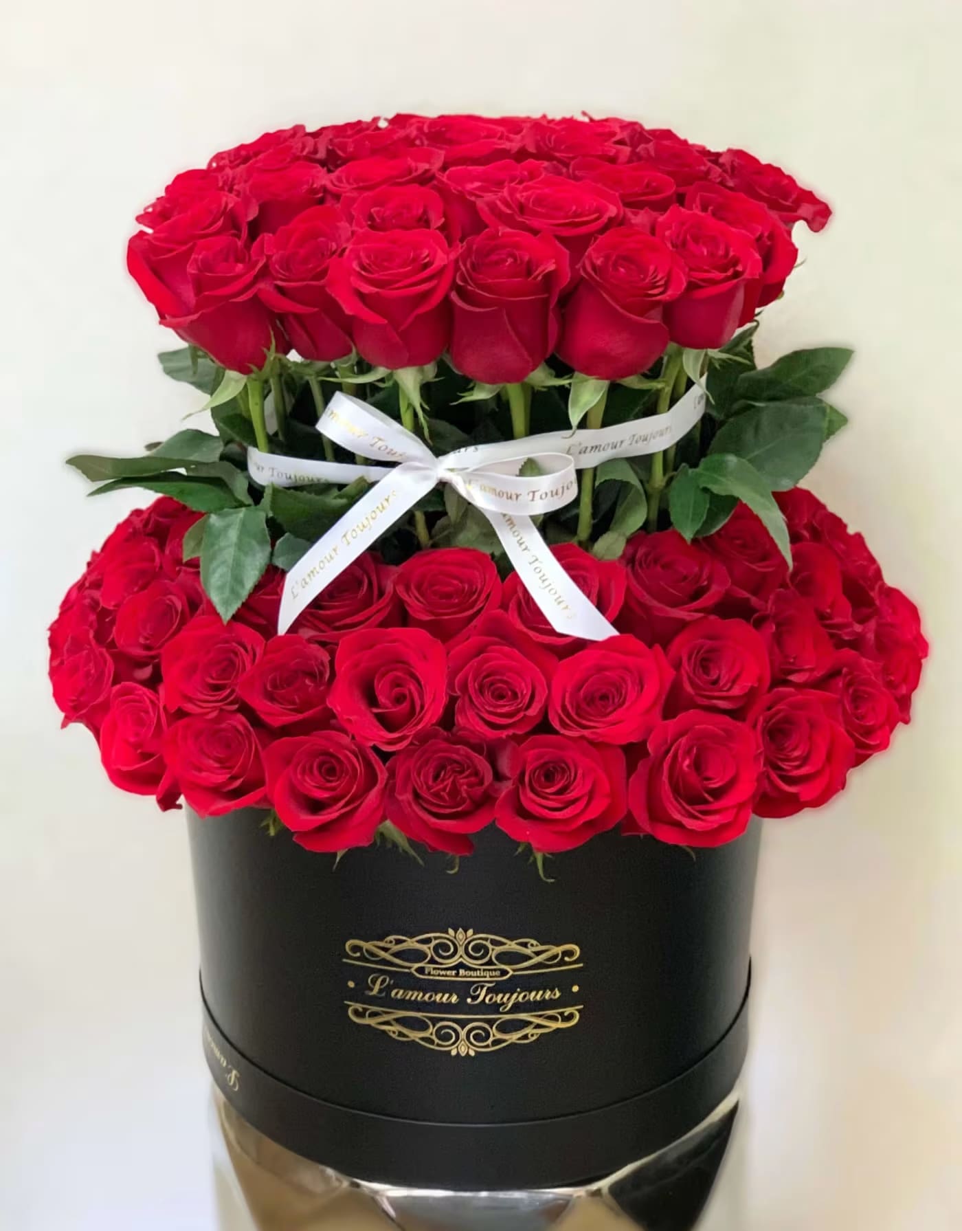 Two tiers of red roses in a black hatbox with a white ribbon
