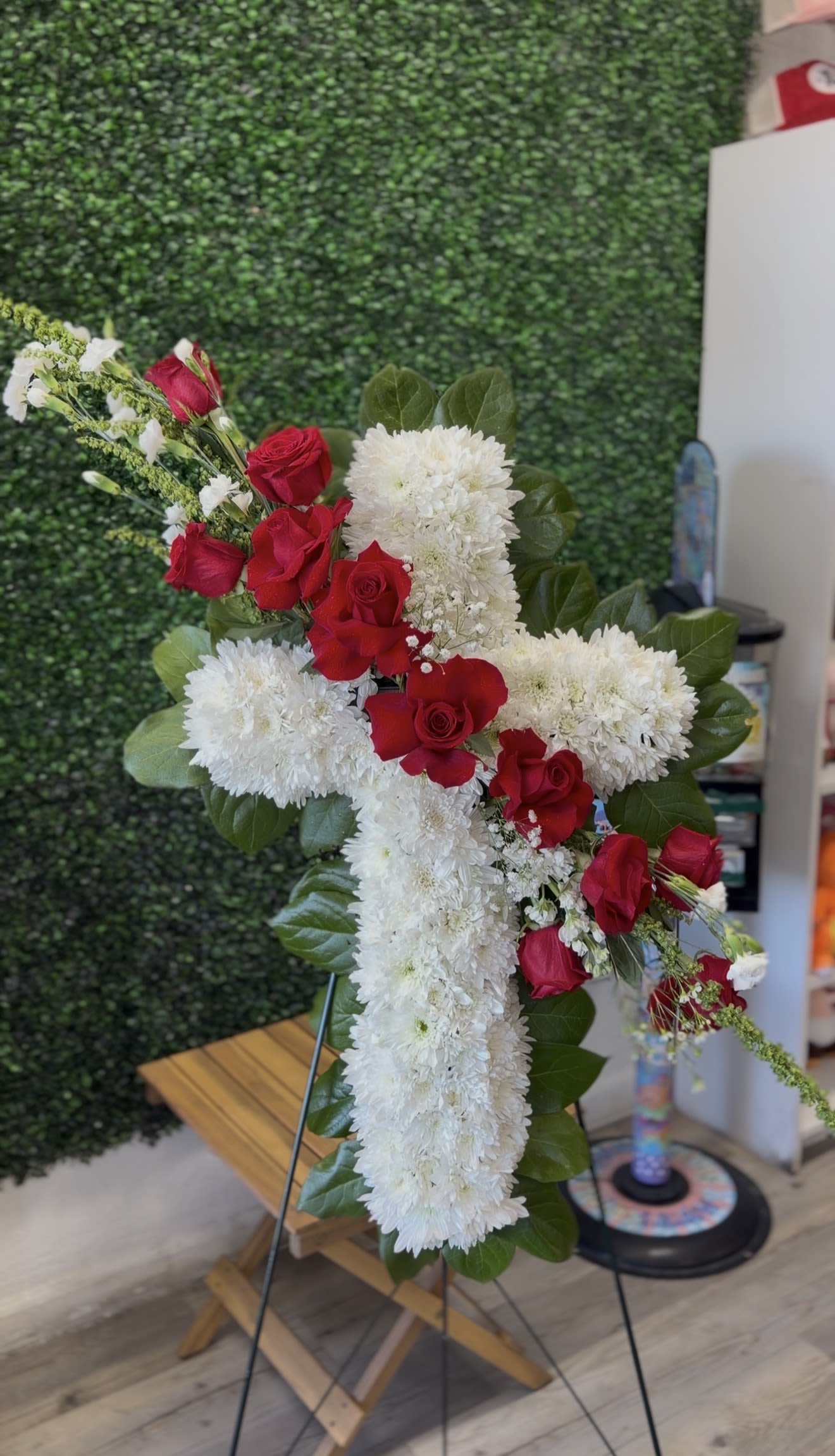 Graceful Remembrance Cross  - A beautiful cross shaped floral tribute designed with soft white chrysanthemums and accented with elegant red rosses. This standing arrangement symbolizes faith, love, and remebreance, making it a meaningful piece for honoring a loved one. 
