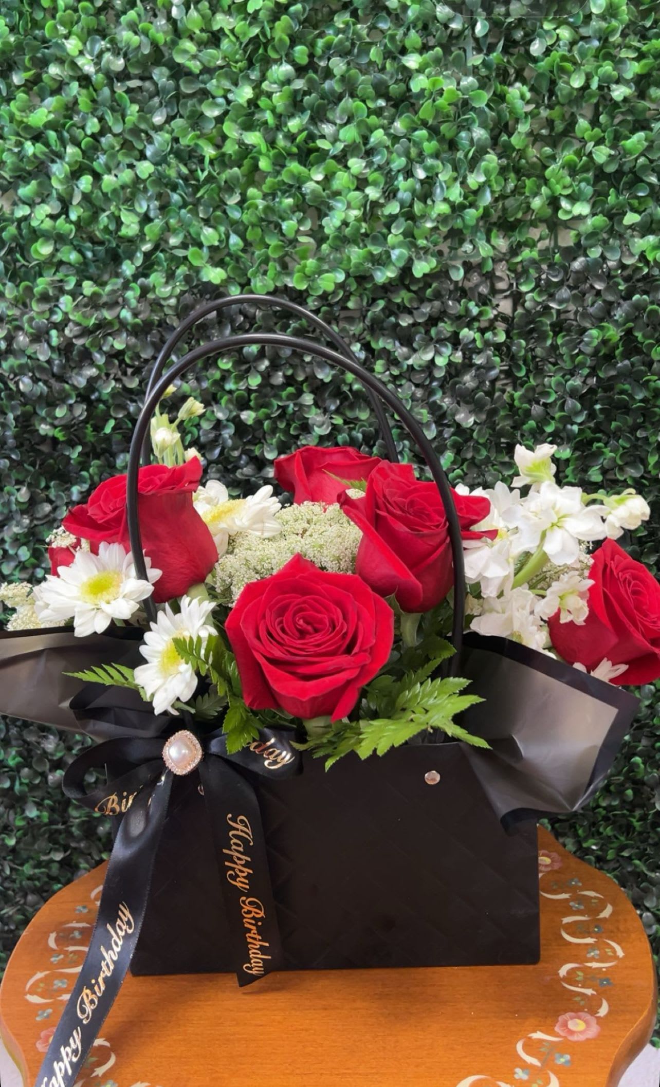 A Purse Full Of Love  - A custom black bag with vibrant, color blooms, featuring red roses, delicate filler flower greenery, finished with a satin bow(please note for any custom work feel free to email, give us a call or walk into our store!)
