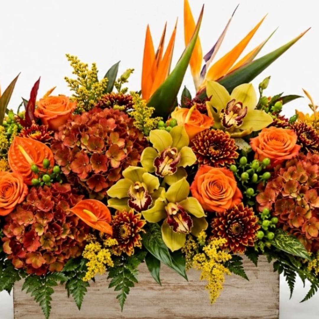 Orange roses and orchids arranged with tropical blooms in a wooden container