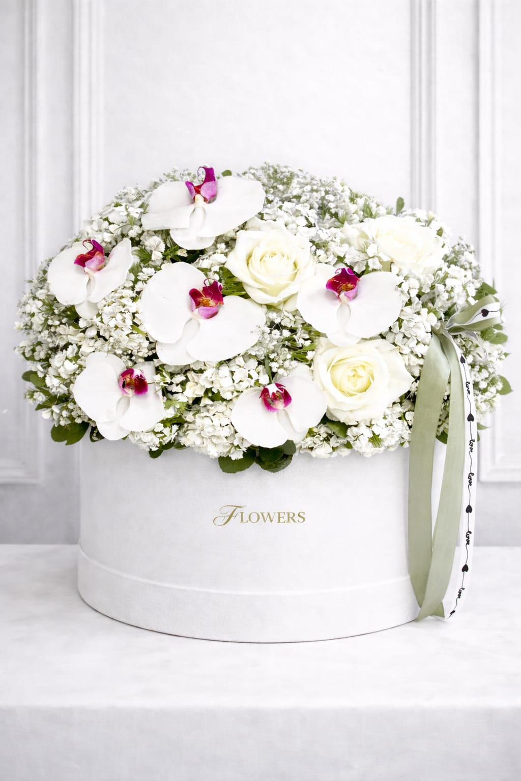 White roses and orchids arranged in a round white box with a ribbon