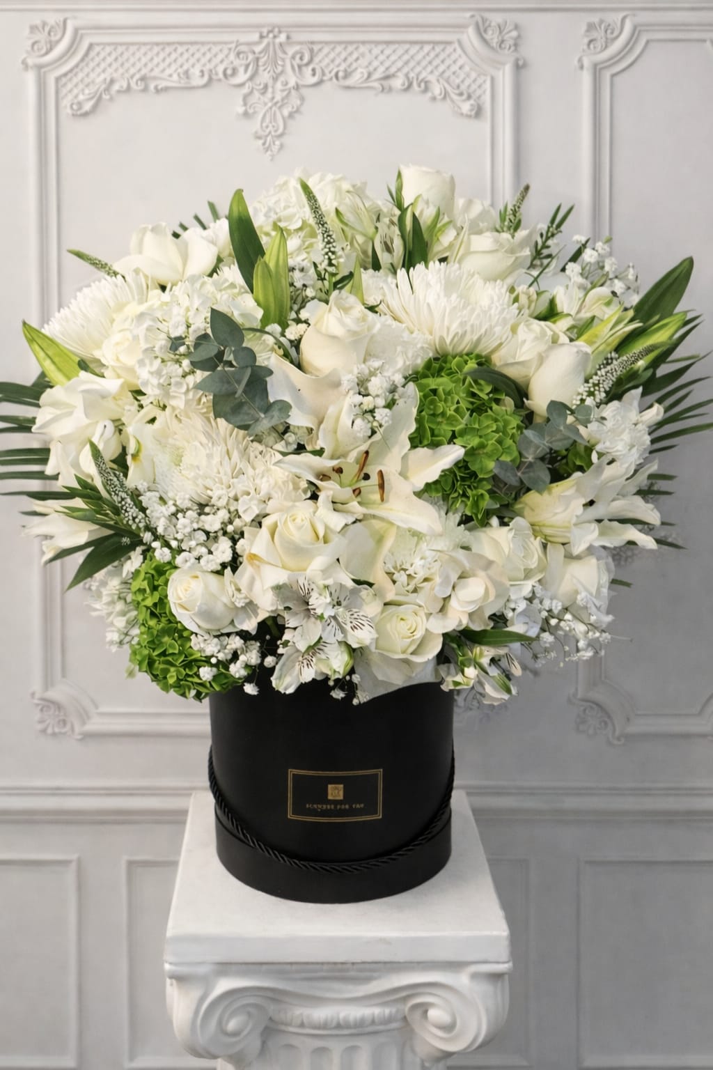 White floral arrangement in a black hat box with green accents