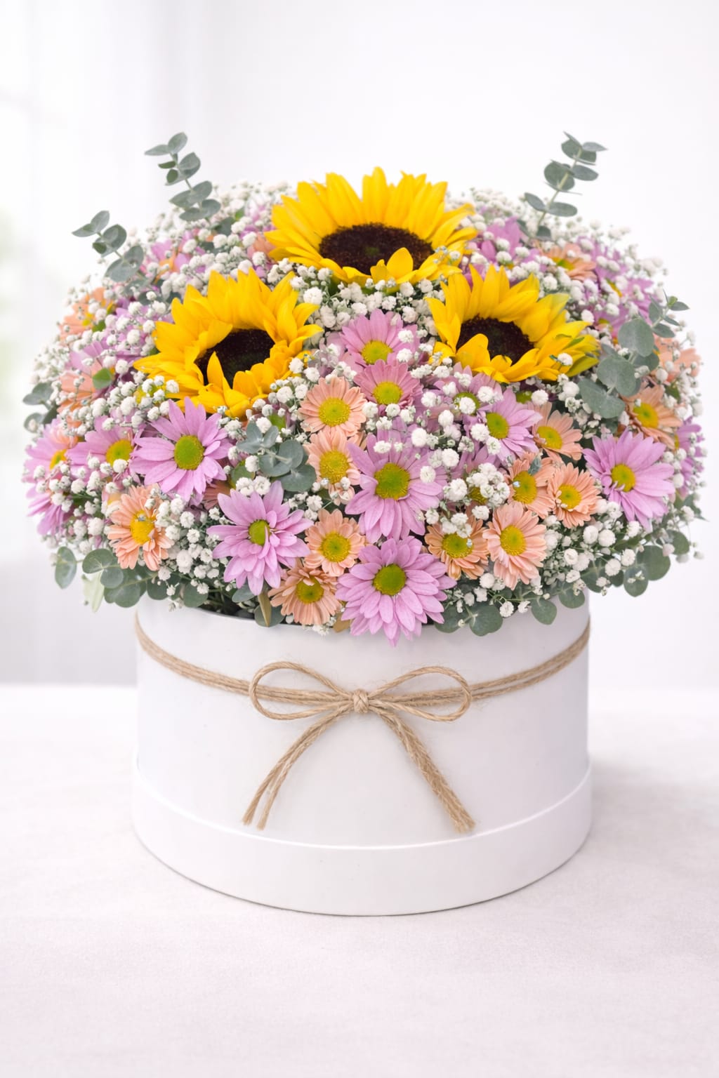 Pastel Spring Garden Box - Welcome spring with our Pastel Spring Garden Box, a bright and cheerful floral arrangement designed to bring warmth and joy. Featuring radiant sunflowers, soft pastel daisies, airy baby’s breath, and fresh eucalyptus, this seasonal bouquet is beautifully arranged in an elegant white hat box.  Perfect for spring birthdays, Mother’s Day, Easter celebrations, thank-you gifts, get-well wishes, or simply brightening someone’s day. Each arrangement is thoughtfully hand-designed with premium fresh flowers by Oh Flower by Naz, your trusted Carlsbad florist.   Available for local flower delivery in Carlsbad and throughout North County San Diego.