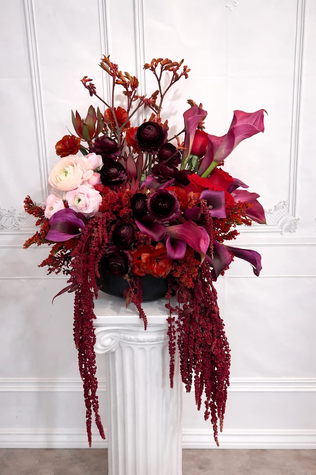 Tall floral arrangement with pink calla lilies, roses, and dark blooms in a black container