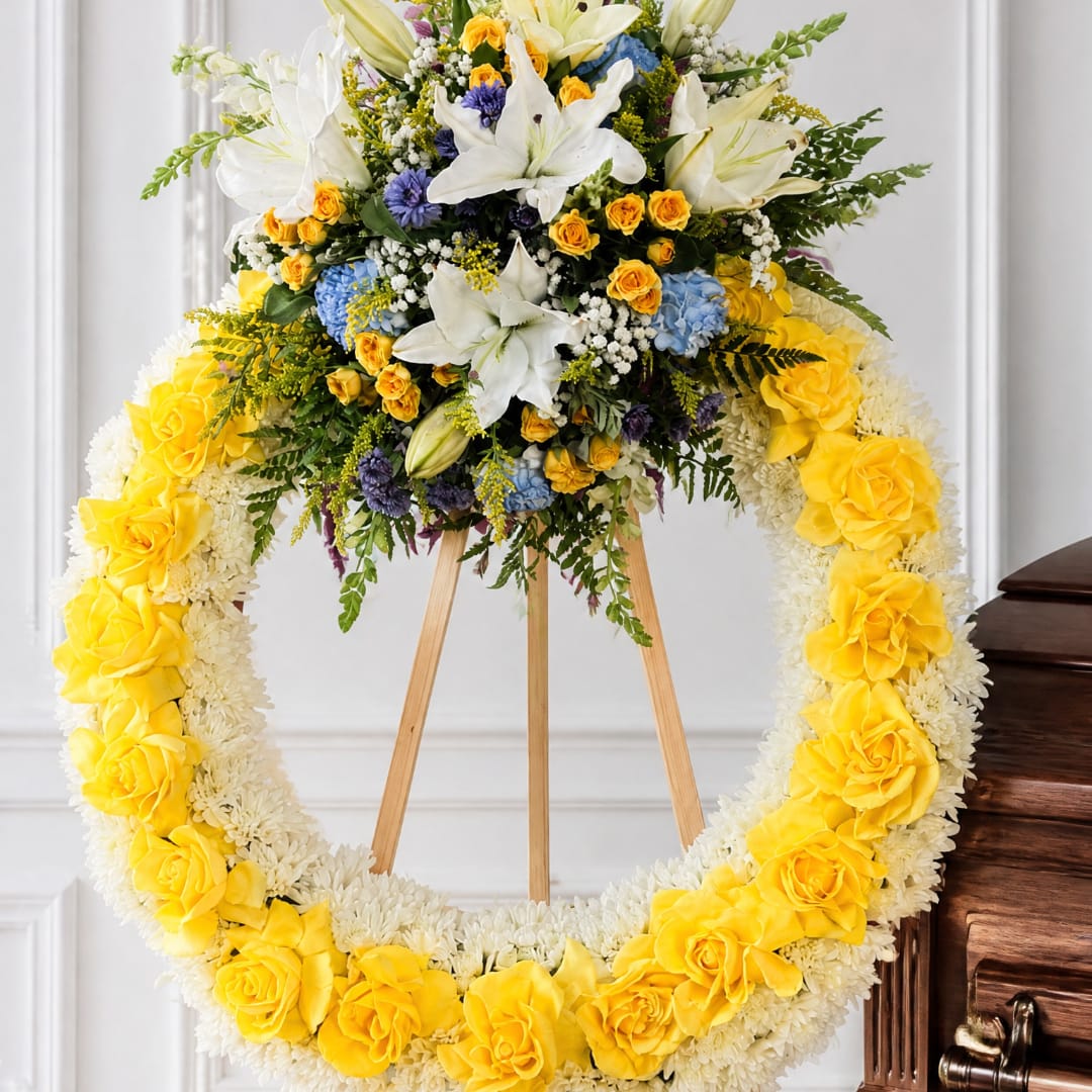 Yellow and white floral funeral wreath on a wooden easel