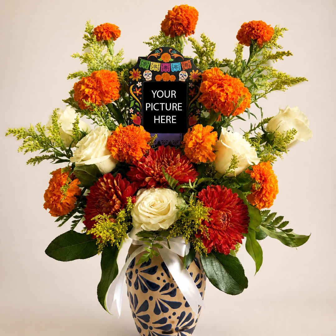 Orange and red flowers arranged in a patterned vase with a photo frame