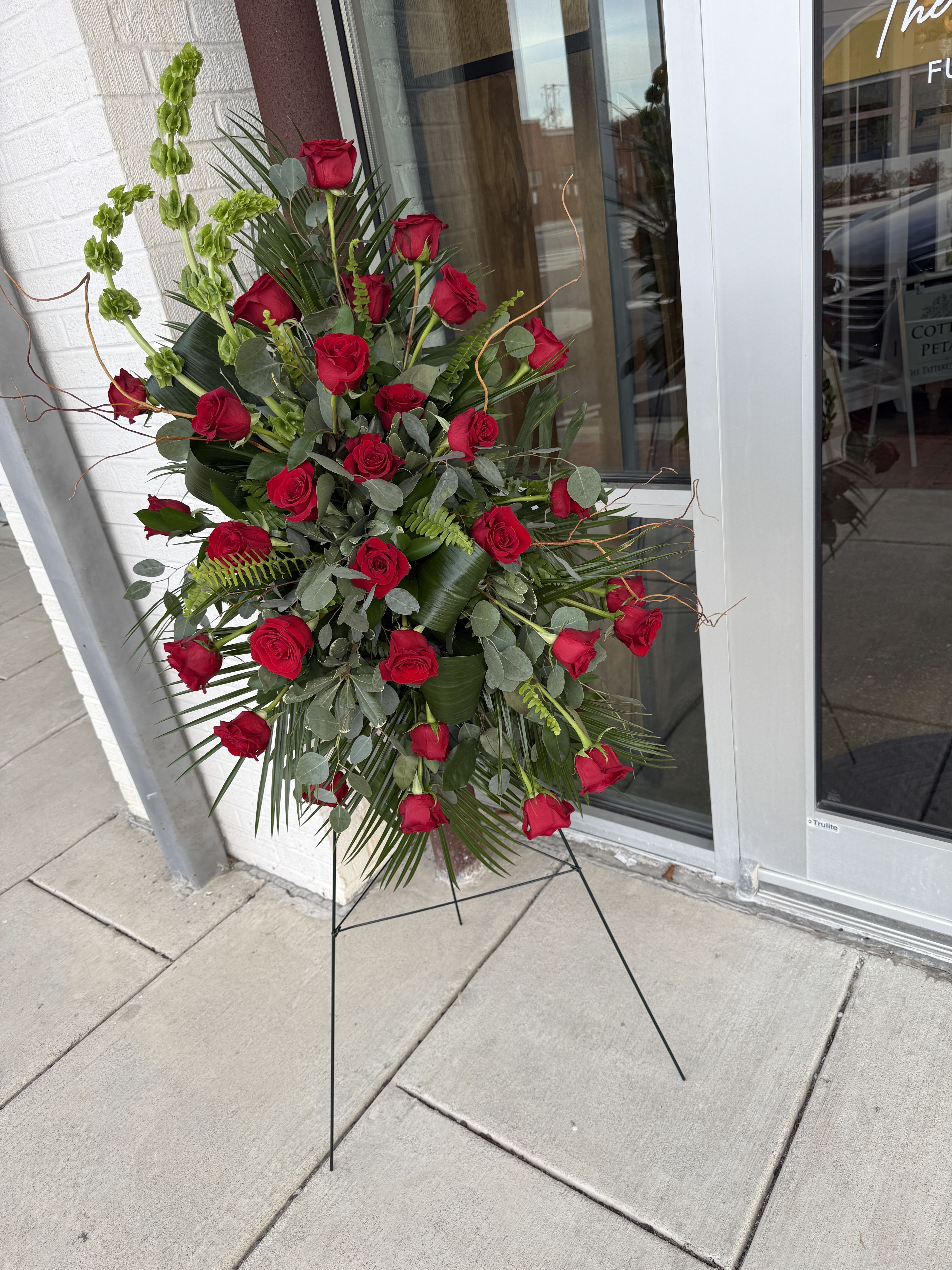 Tall standing arrangement of red roses with greenery on a metal easel
