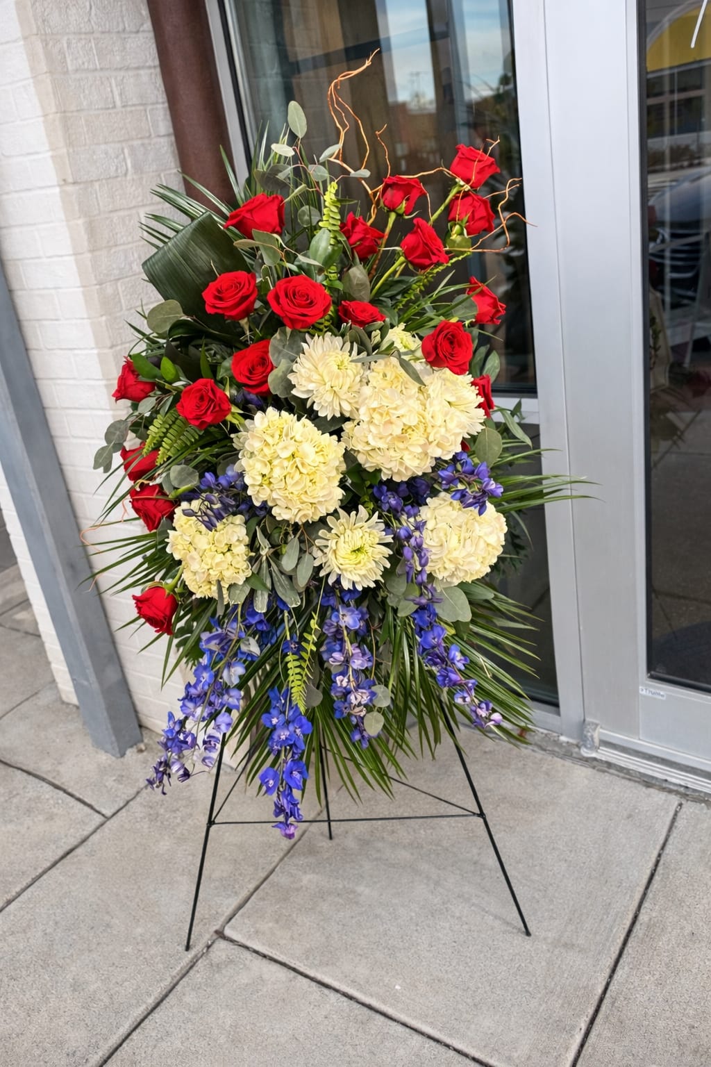 Standing floral spray with red roses, cream blooms, and blue orchids