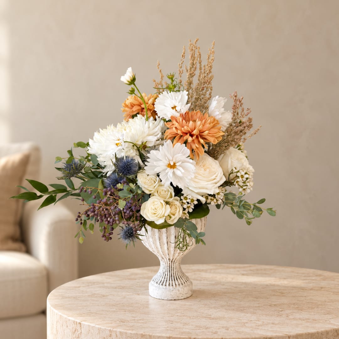 White and peach floral arrangement in a white pedestal vase
