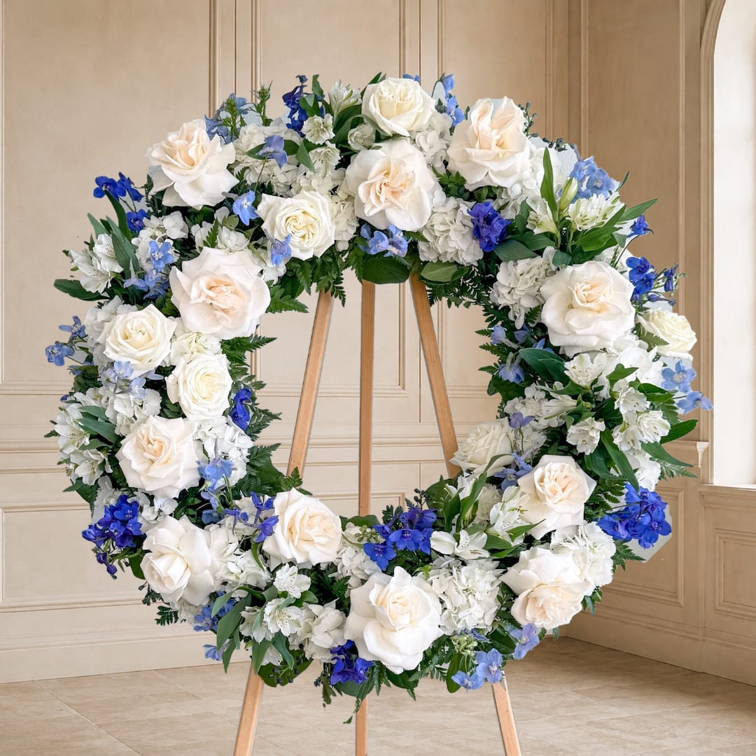 Large white and blue floral wreath on a wooden stand