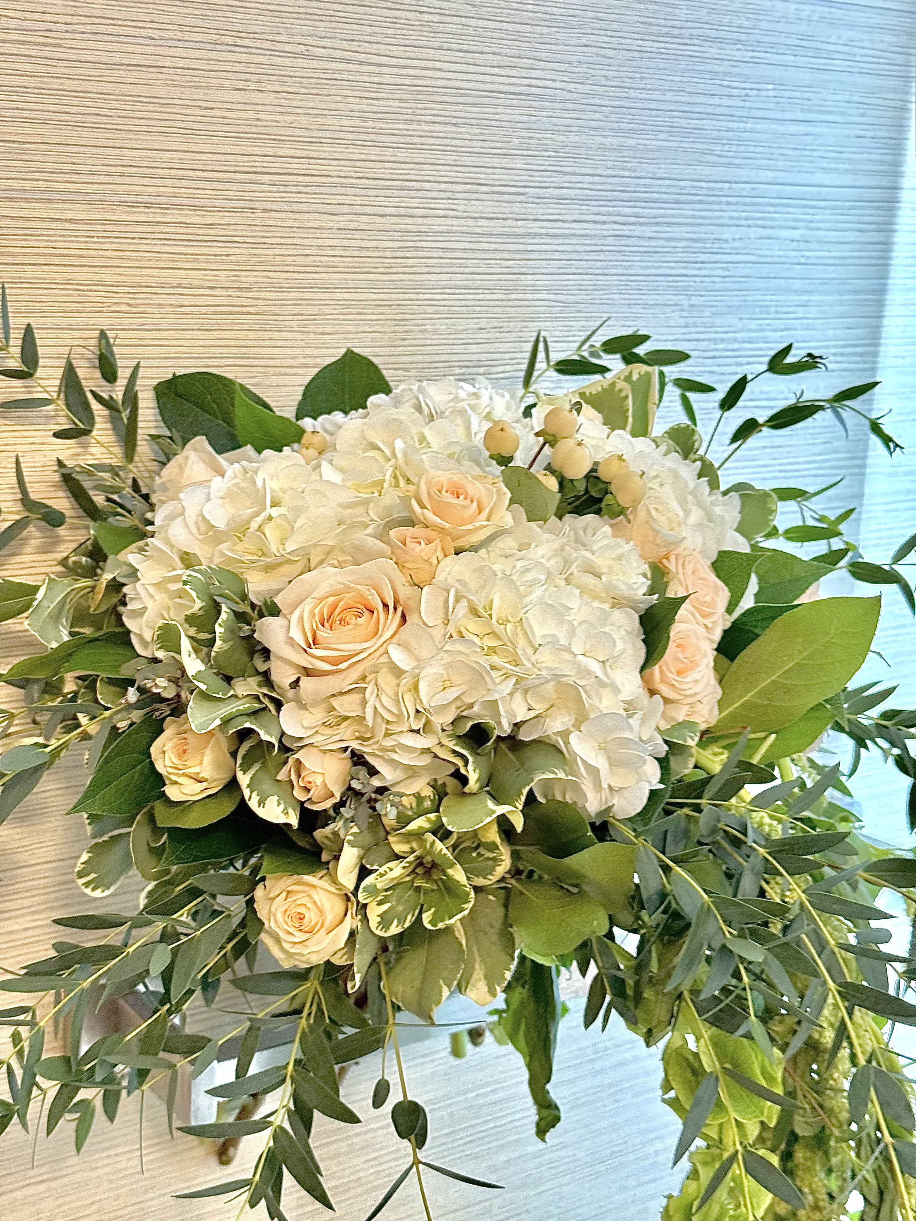 White hydrangeas and peach roses in a lush bouquet with greenery