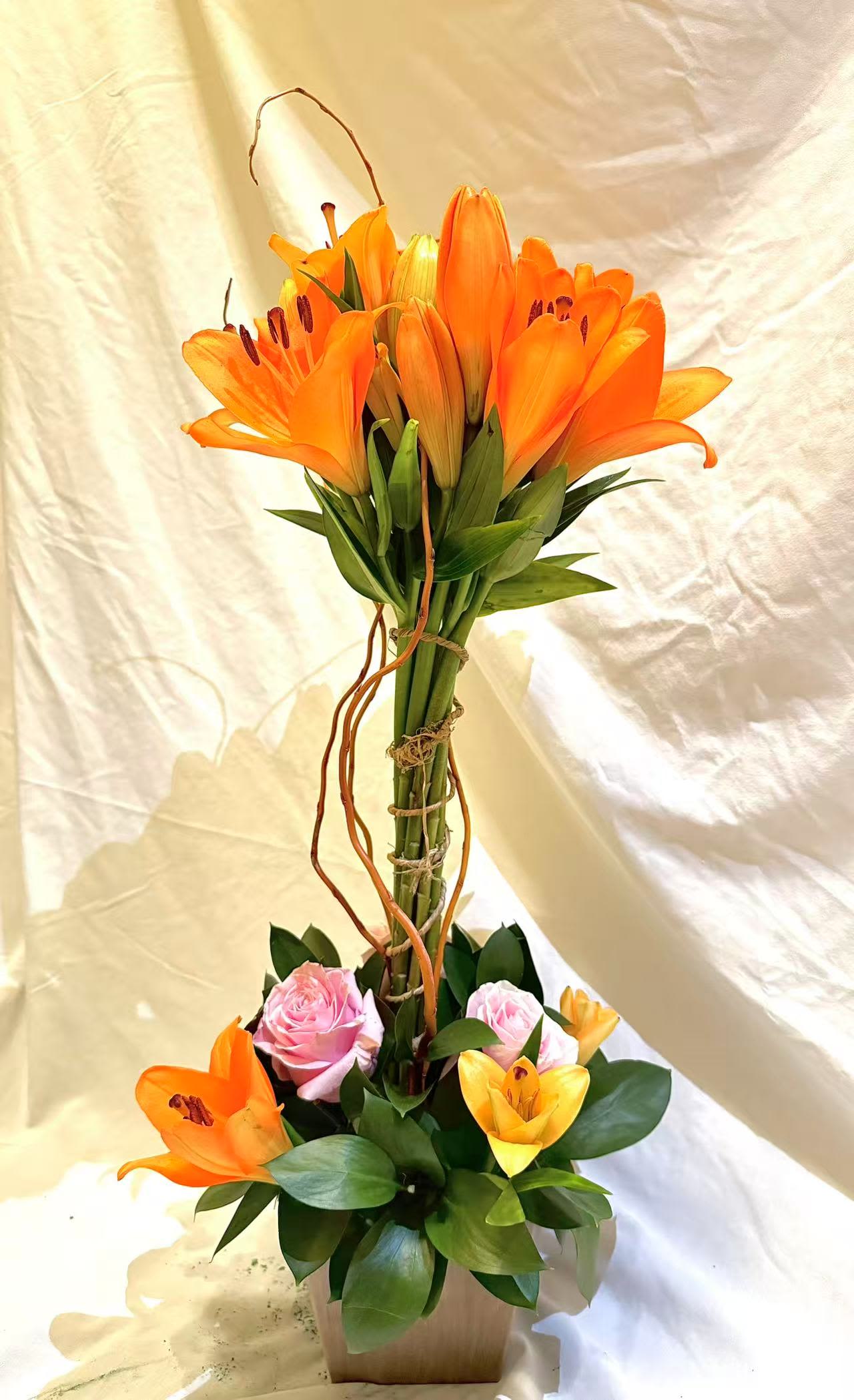 Orange lilies and pink roses arranged in a tall vase