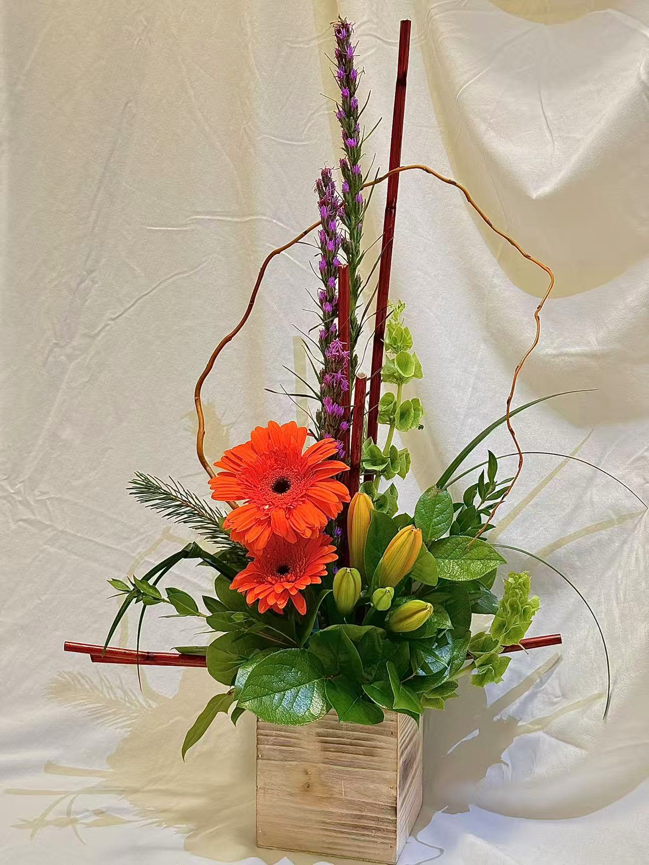 Orange gerbera daisies in a wooden box with purple spikes and green buds