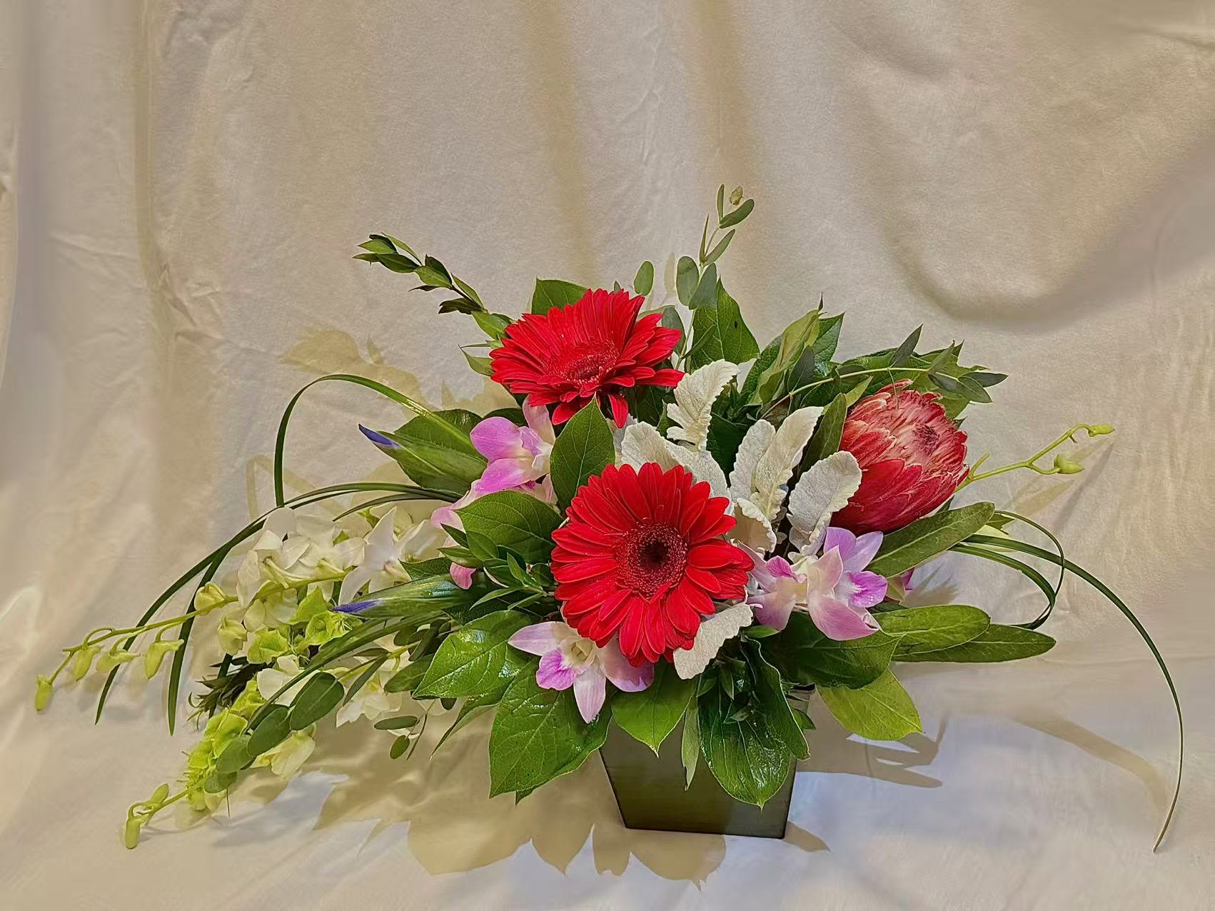 Red gerbera daisies and pink orchids in a low rectangular vase
