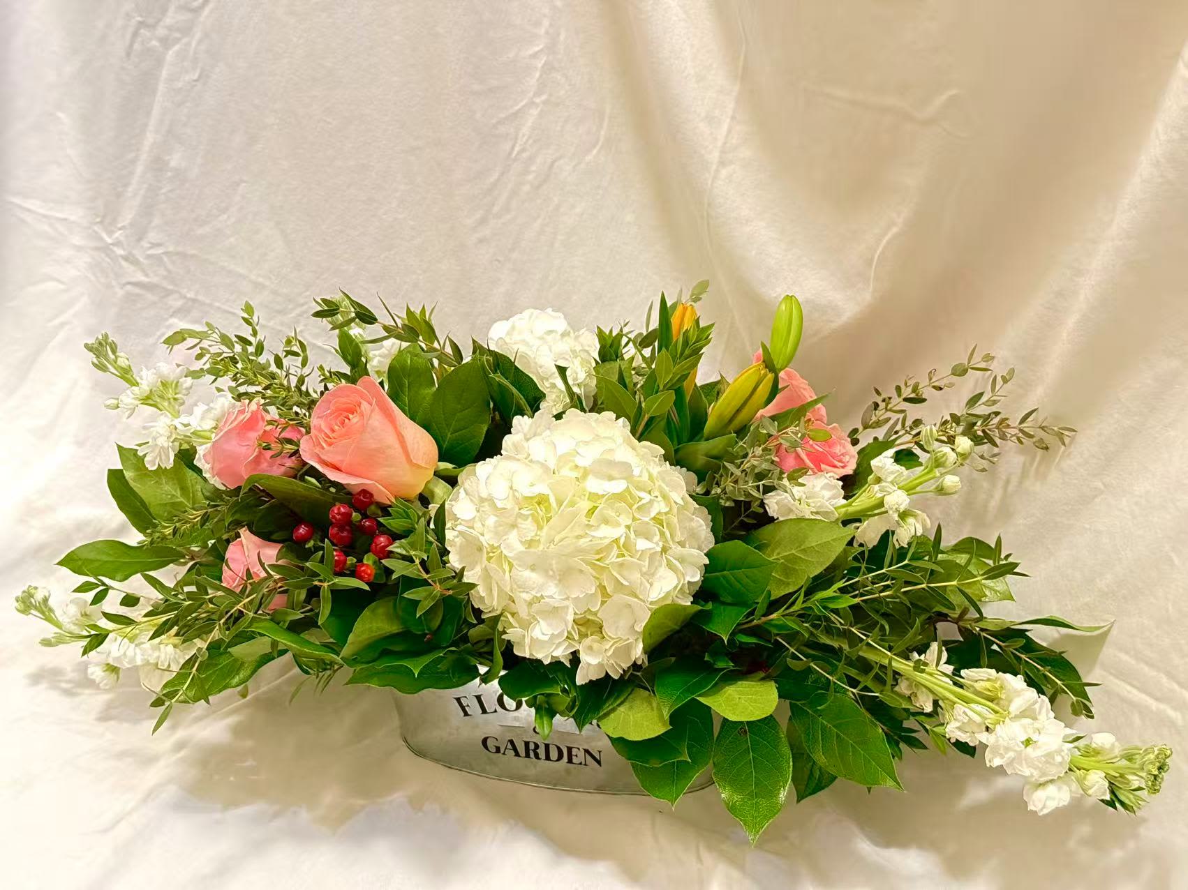 Blush Garden Harmony - A soft garden-style floral arrangement featuring lush white hydrangeas, blush roses, delicate white stock, seasonal berries, and fresh greenery. Designed in a low, elongated silhouette, this piece offers a natural, airy look that brings warmth and elegance to any space.  Perfect for weddings and special celebrations, as well as everyday home décor, dining tables, and thoughtful gifts. Each arrangement is handcrafted with premium seasonal blooms and may vary slightly while maintaining the same color palette, garden style, and overall aesthetic.