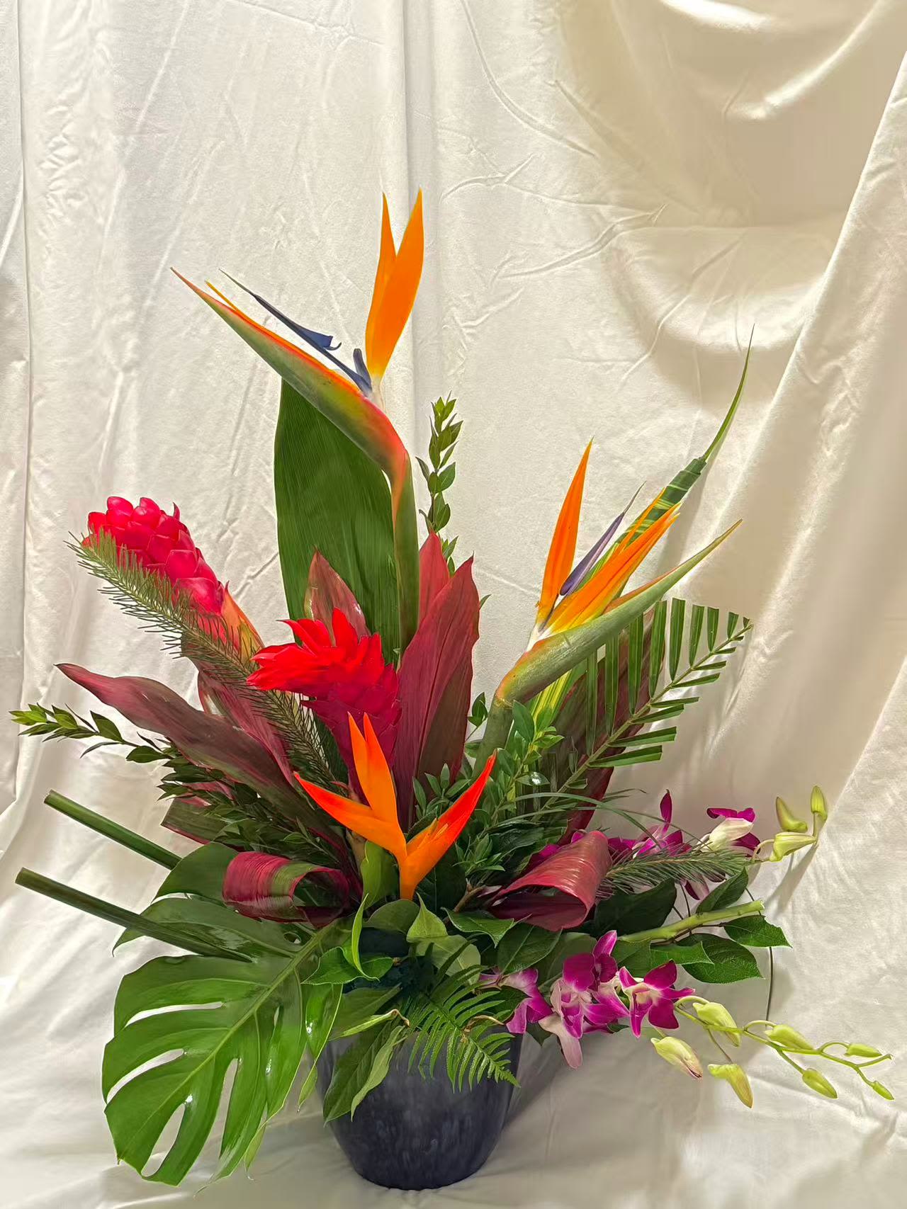 Tropical flower arrangement with bird of paradise and orchids in a dark vase