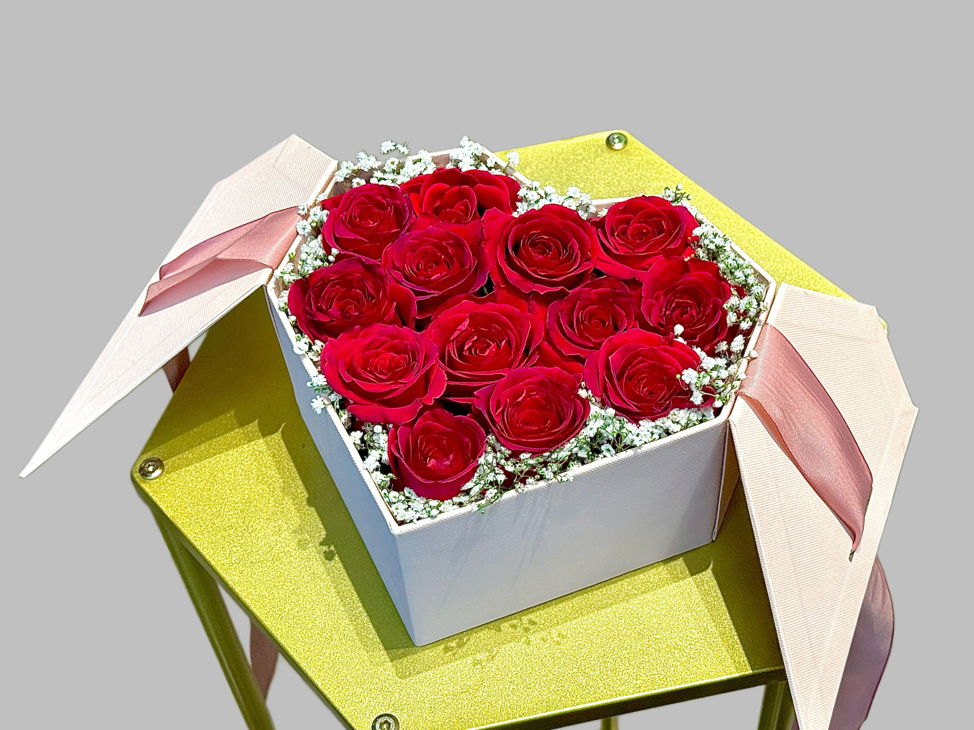 Box of red roses with pink ribbons on a gold stand