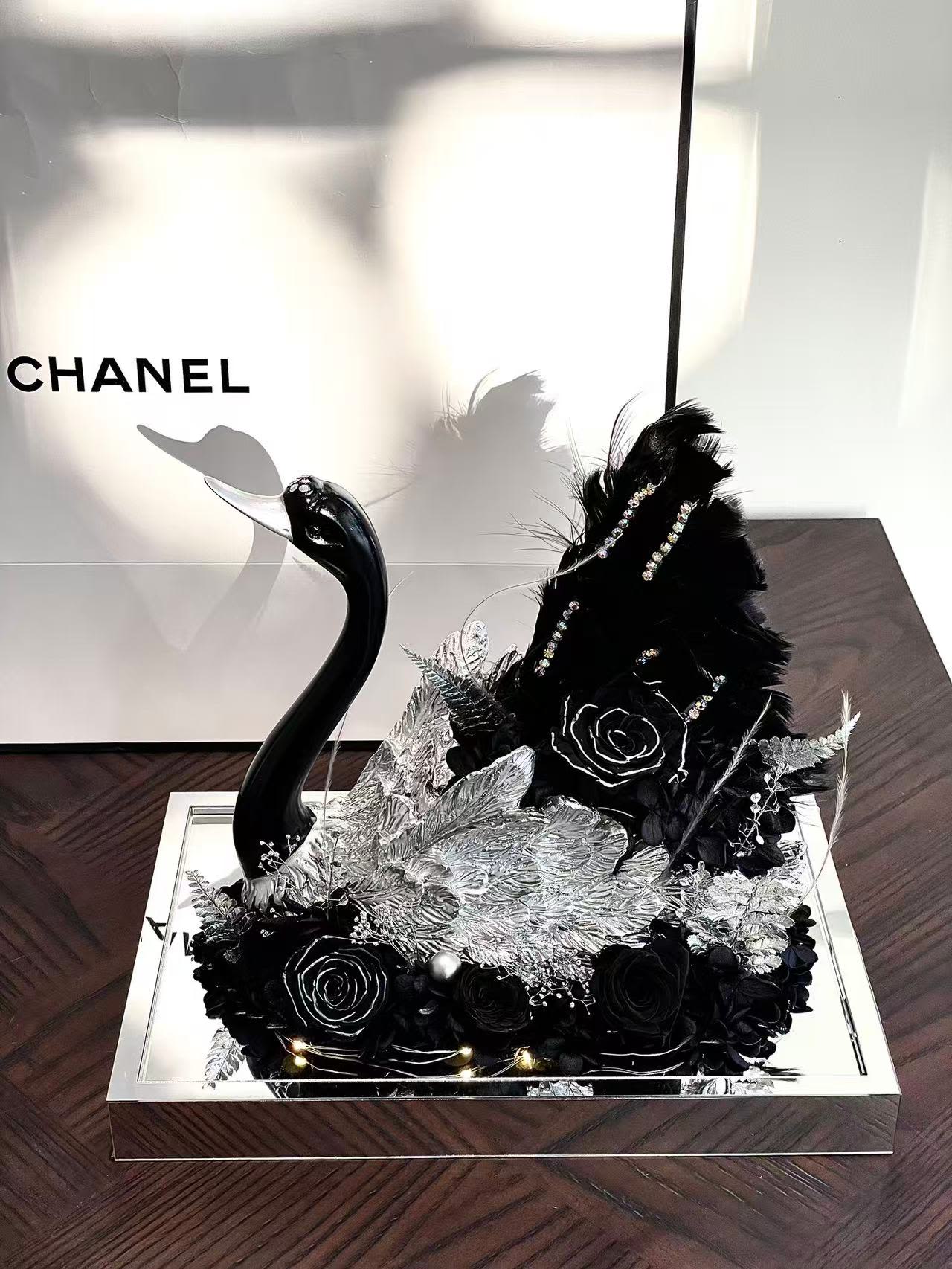 Black floral arrangement with a swan figurine in a mirrored tray