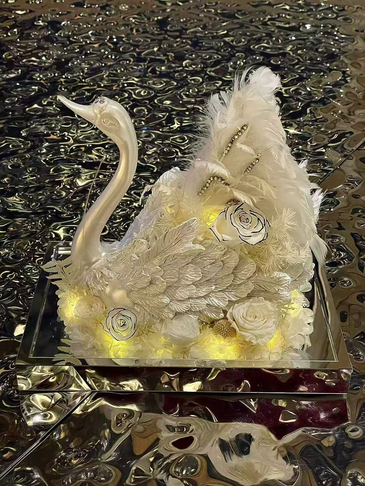 White floral swan sculpture with feathers and roses on a mirrored base