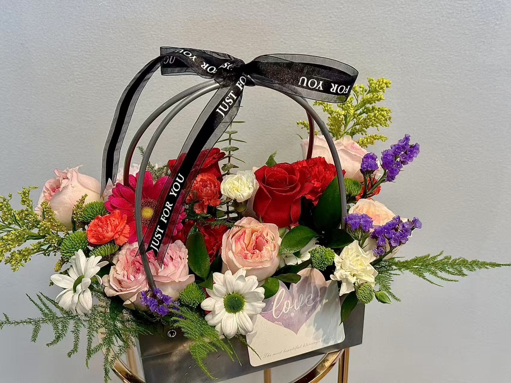 Mixed flower arrangement in a black handled basket with a ribbon bow