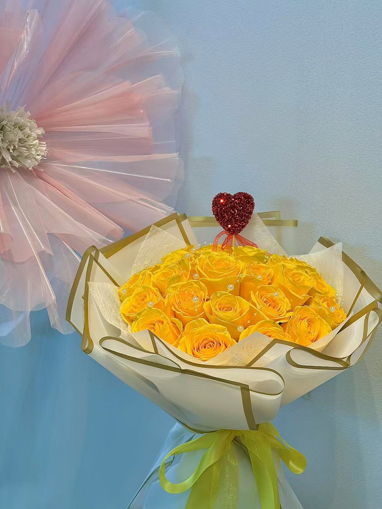 Bouquet of yellow roses wrapped in white paper with a red heart topper