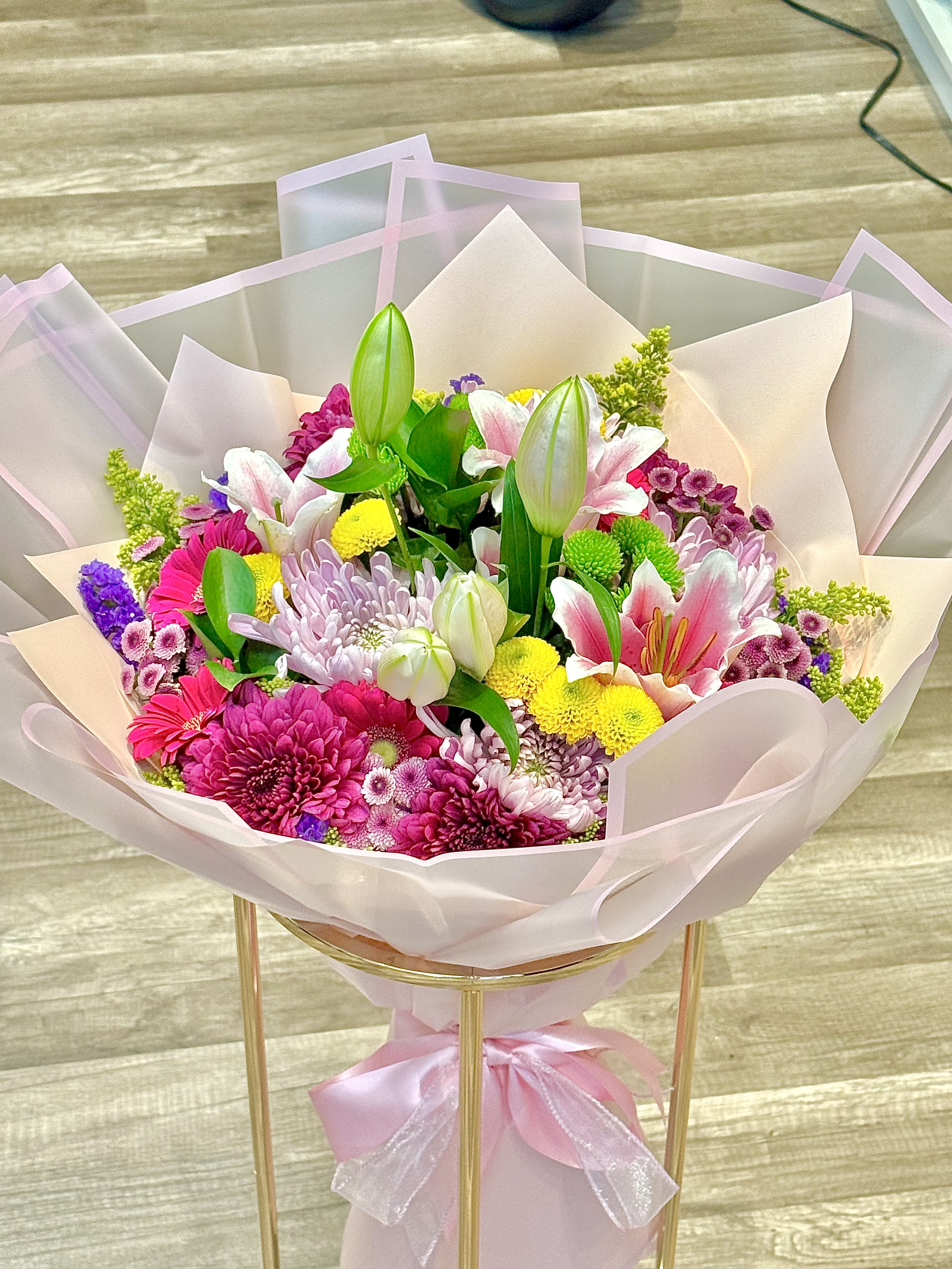 Bouquet of pink, white, and yellow flowers wrapped in pale pink paper