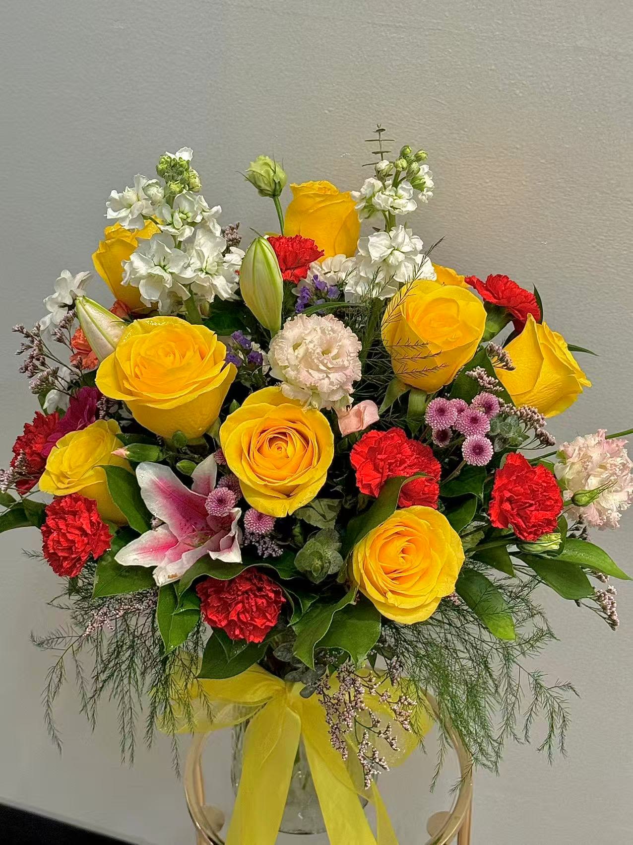 Bouquet of yellow roses, red carnations, and white flowers in a clear vase