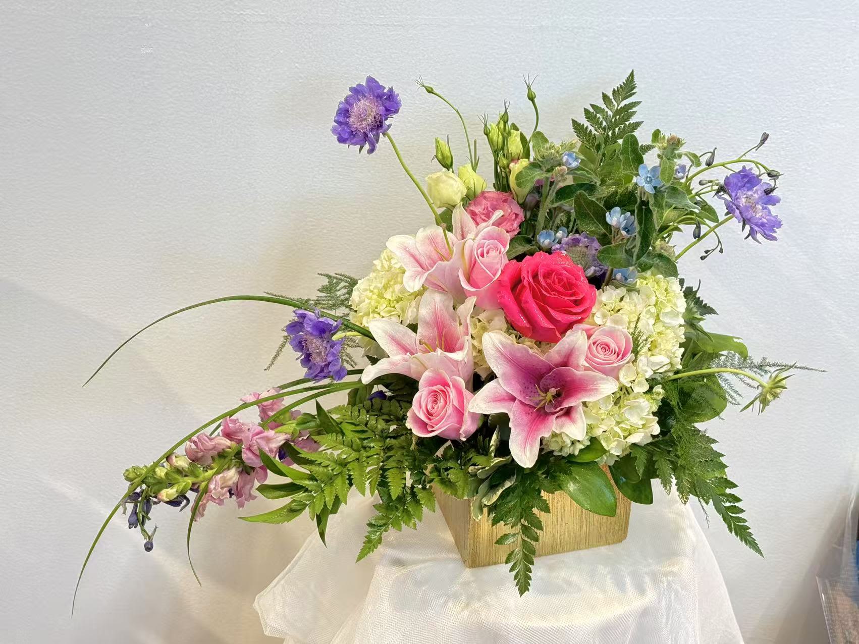 Pink roses and lilies arranged in a wooden container with purple accents