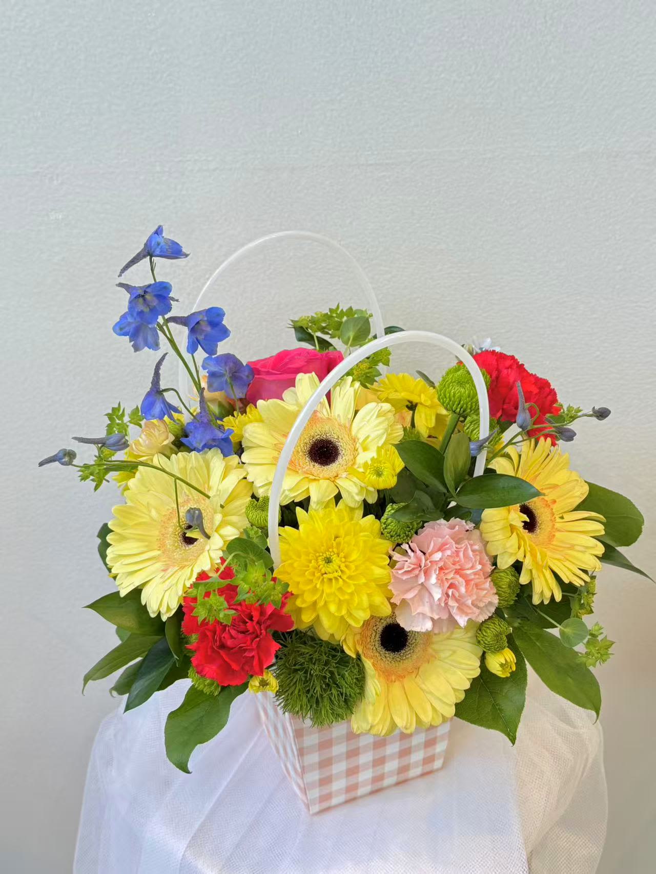 Sunny Garden Flower Basket - A cheerful flower basket featuring bright gerbera daisies, carnations, chrysanthemums, and fresh seasonal blooms. Designed in a charming basket, this colorful arrangement is perfect for celebrations, thank-you gifts, or simply bringing joy to someone's day.