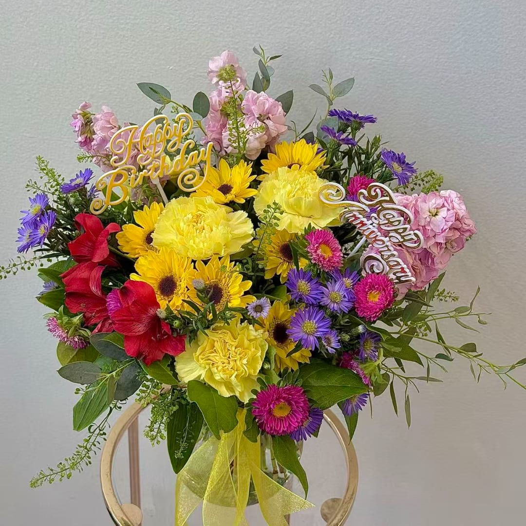 Colorful birthday bouquet with yellow, pink, purple, and red flowers in a glass vase