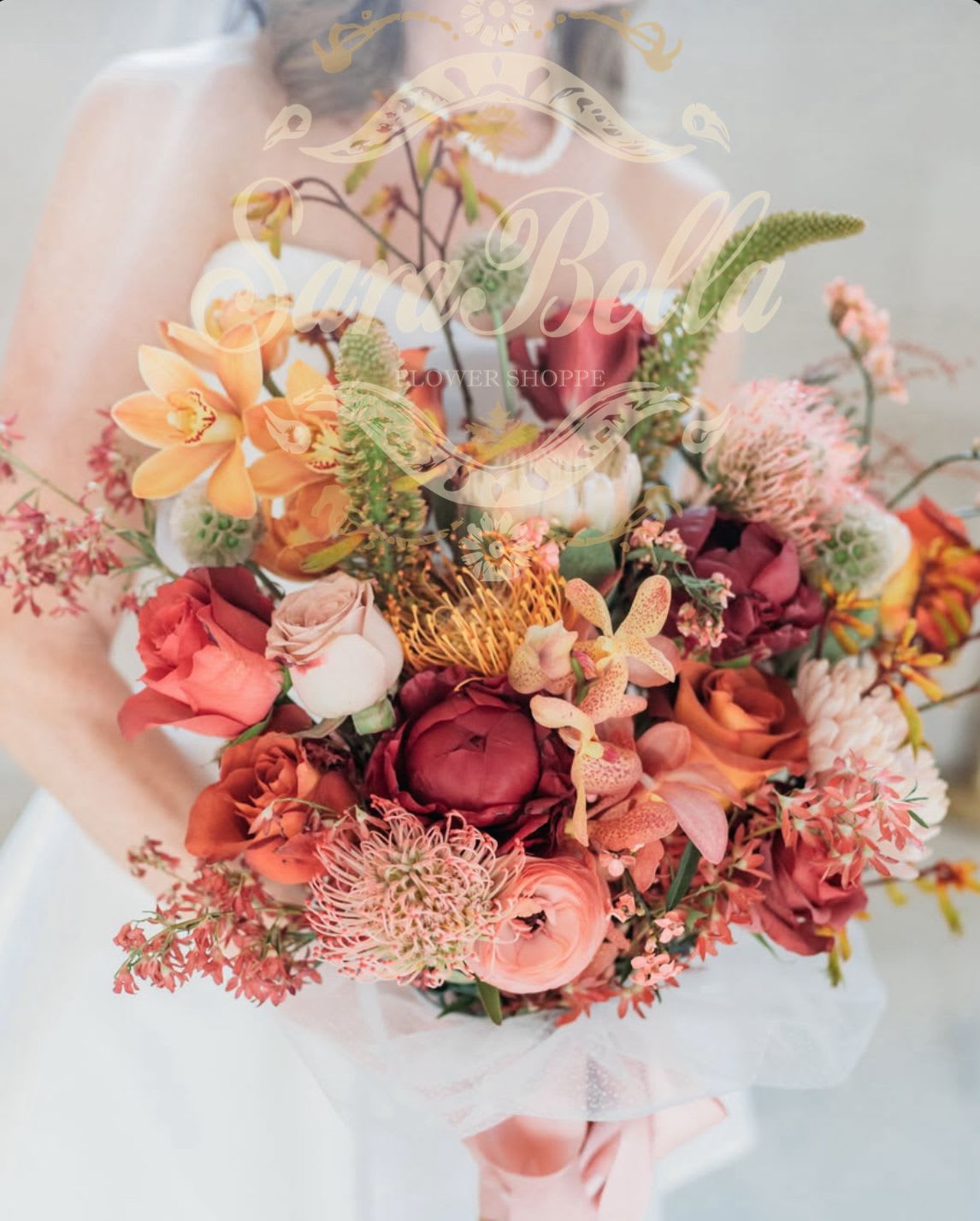 Handheld bouquet of orange, pink, and burgundy flowers