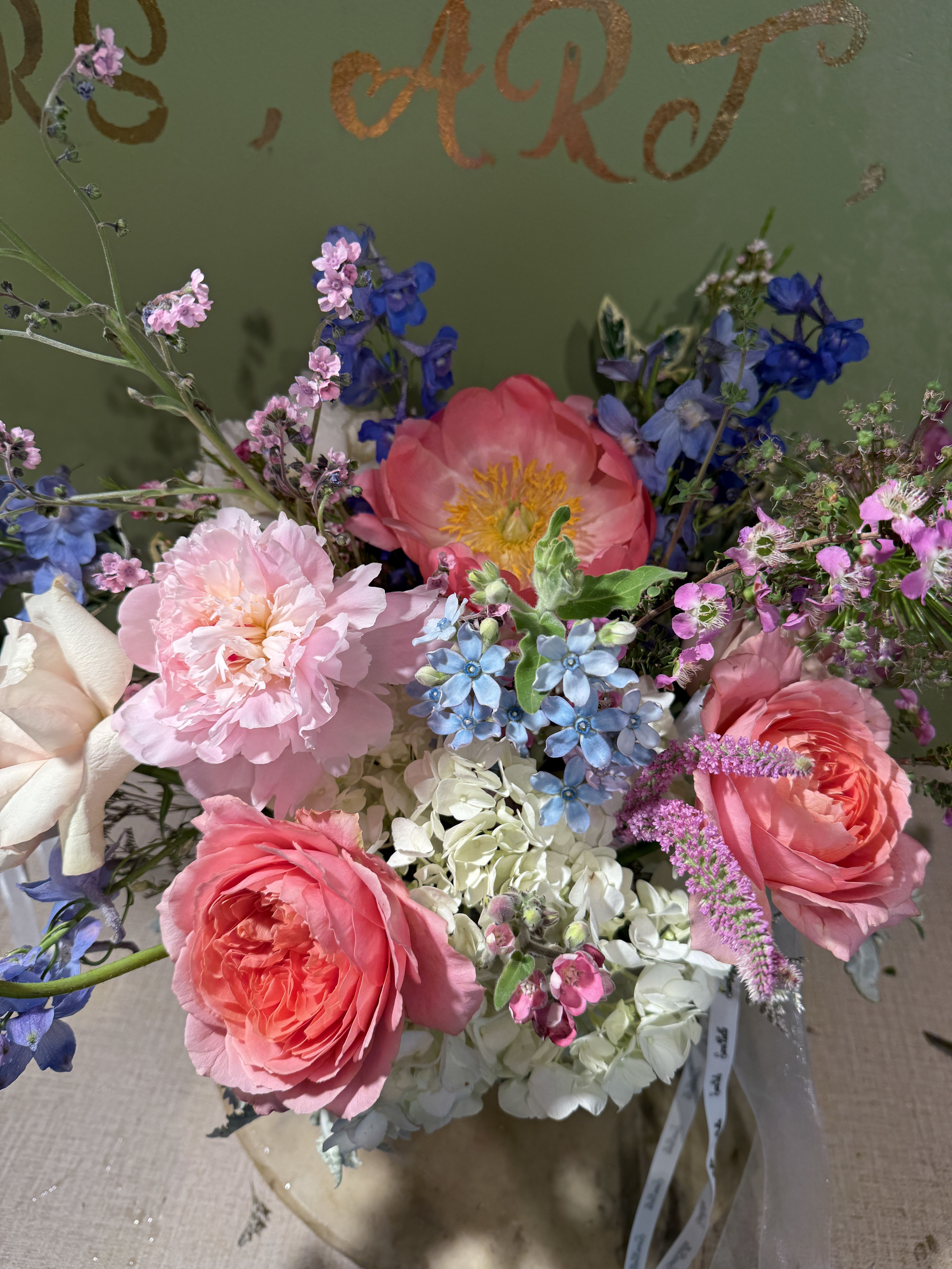 Bouquet of pink roses, peonies, and blue flowers in a wrapped arrangement