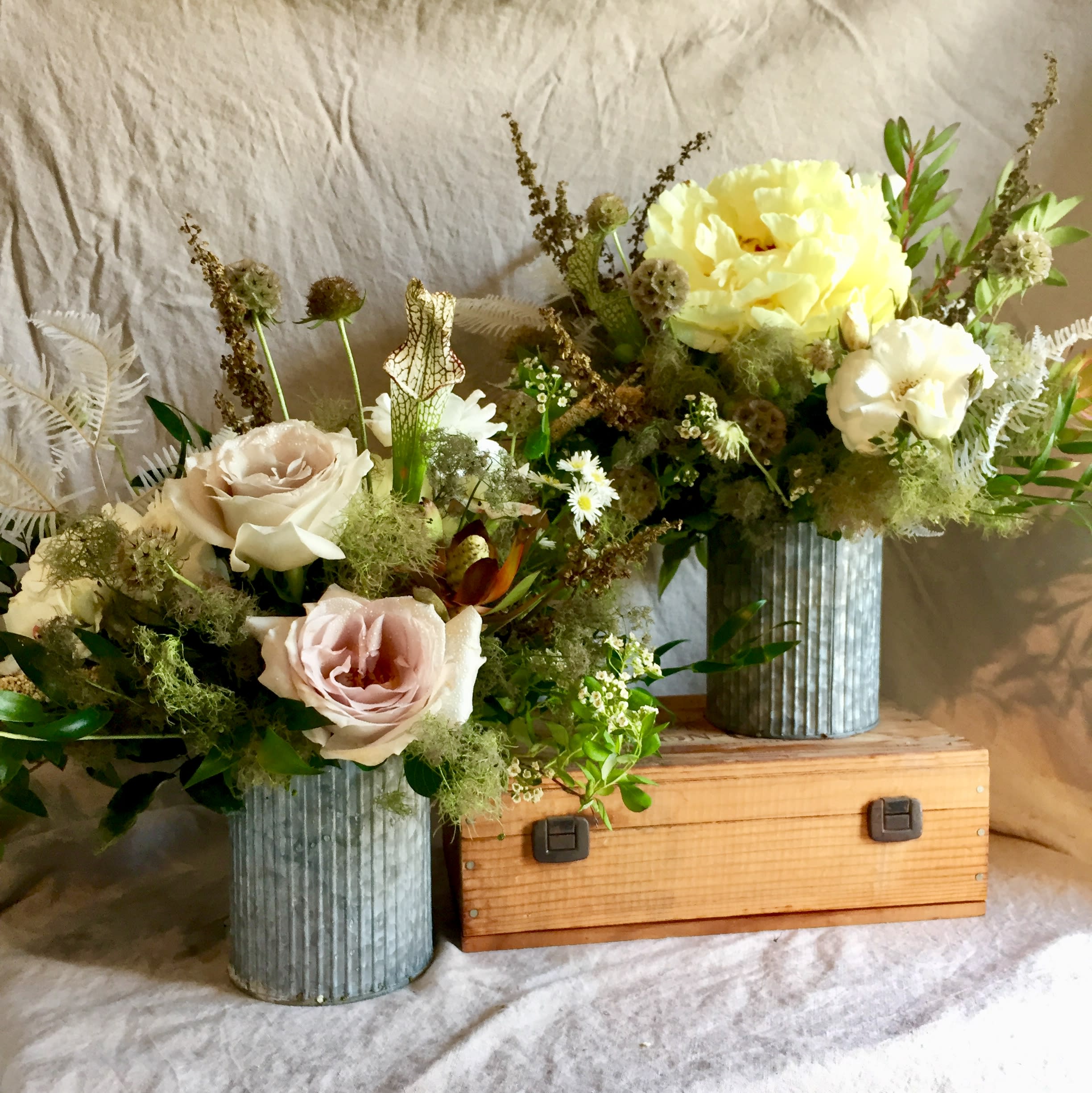 Two floral arrangements in ribbed metal vases with pale roses and yellow blooms