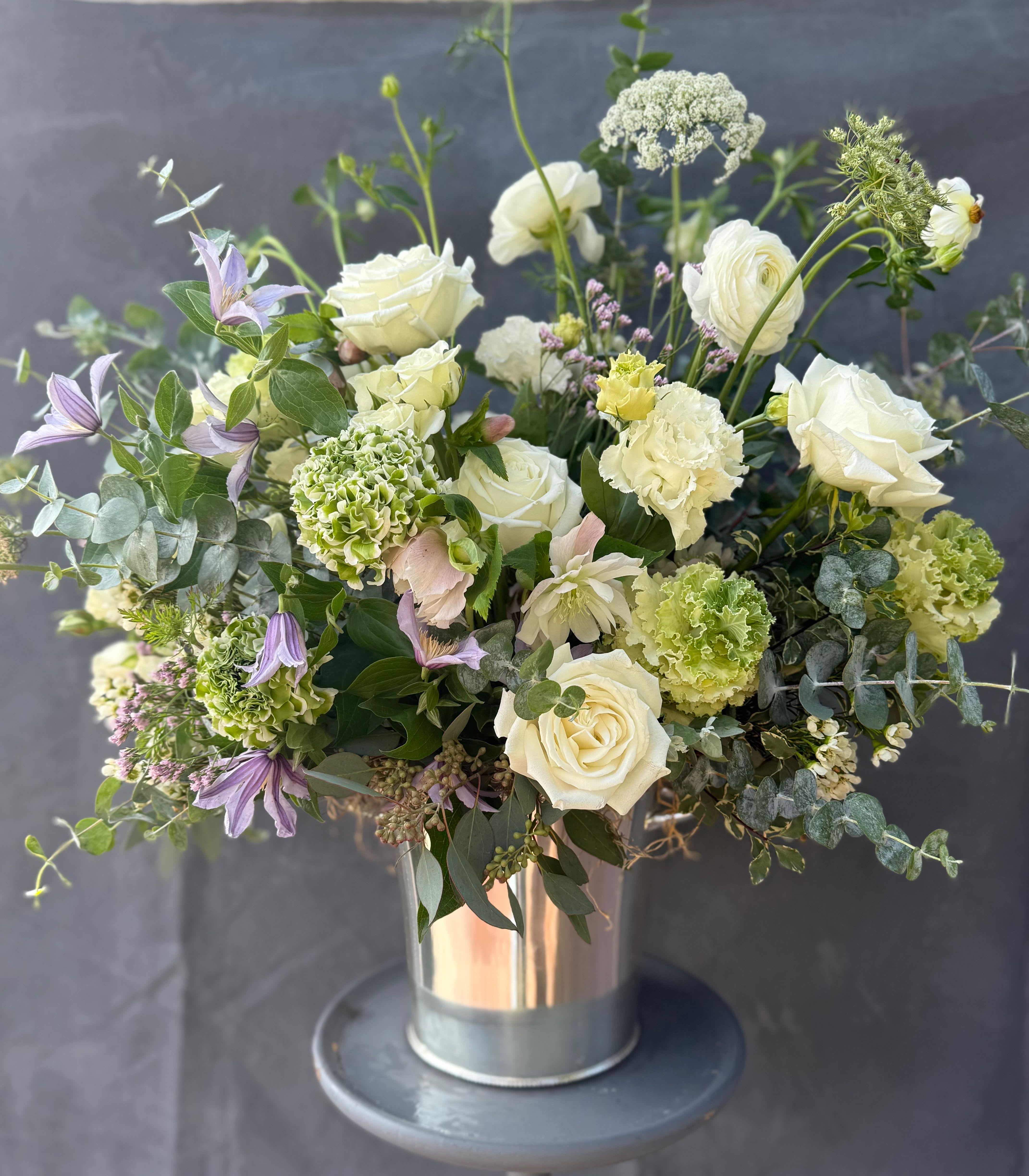 White roses and green blooms in a metal vase with purple flowers