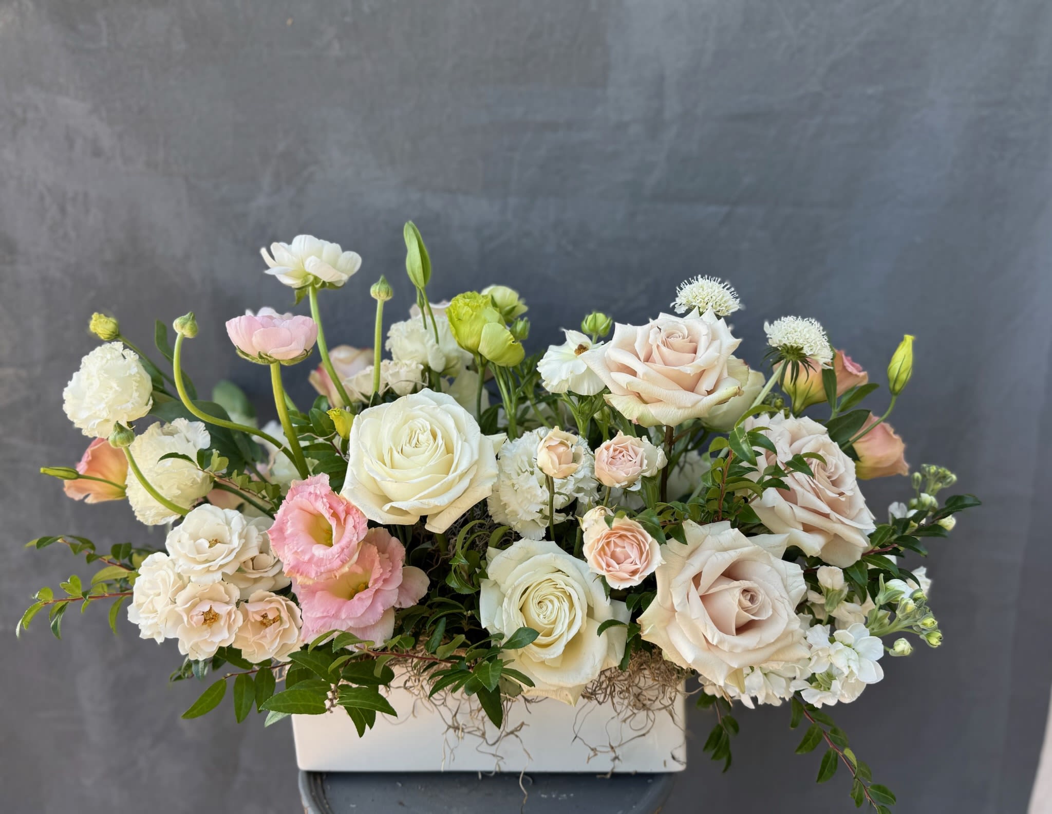 Pastel roses and mixed blooms arranged in a white rectangular vase