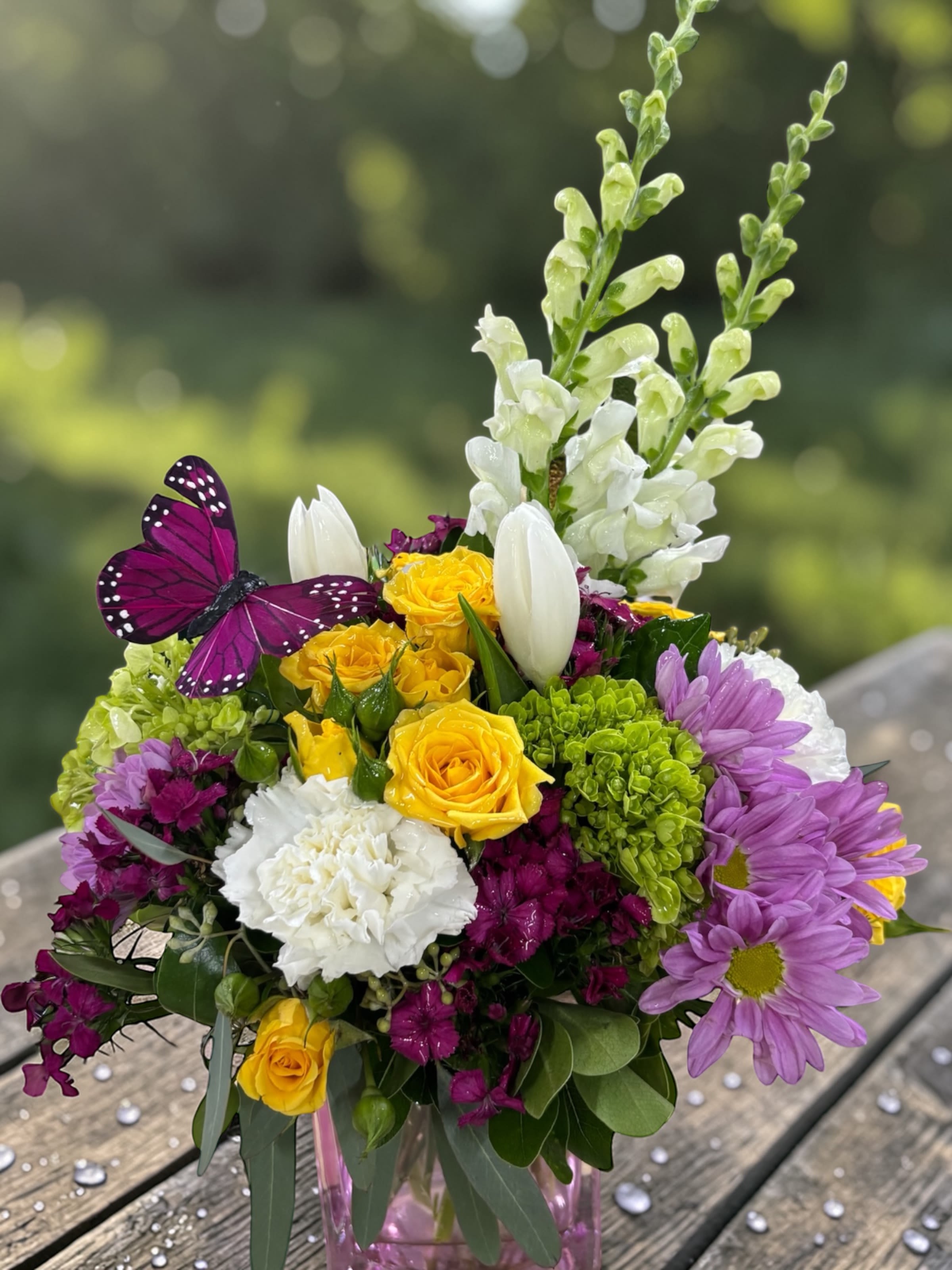 Butterfly Sunrise - A burst of morning sunshine in a vase, this vibrant design brings together yellow roses, crisp white snapdragons, magenta accents, lime hydrangea, and soft lavender daisies for a look that feels bright, fresh, and full of life.  There’s a playful balance here—bold color without chaos, texture without clutter—finished with a butterfly accent that adds a light, cheerful touch without feeling overdone.  Perfect for birthdays, get well, thank-you gifts, thinking of you, or simply sending something to lift someone’s day.  Each arrangement is designed with the freshest seasonal stems available. Colors and varieties may vary slightly to ensure the best overall look.  Available for local flower delivery through Aspen Tower Florist, serving Shelbyville and Greensburg along with Rushville, Batesville, Westport, Oldenburg, St. Paul, Waldron, and Milroy.