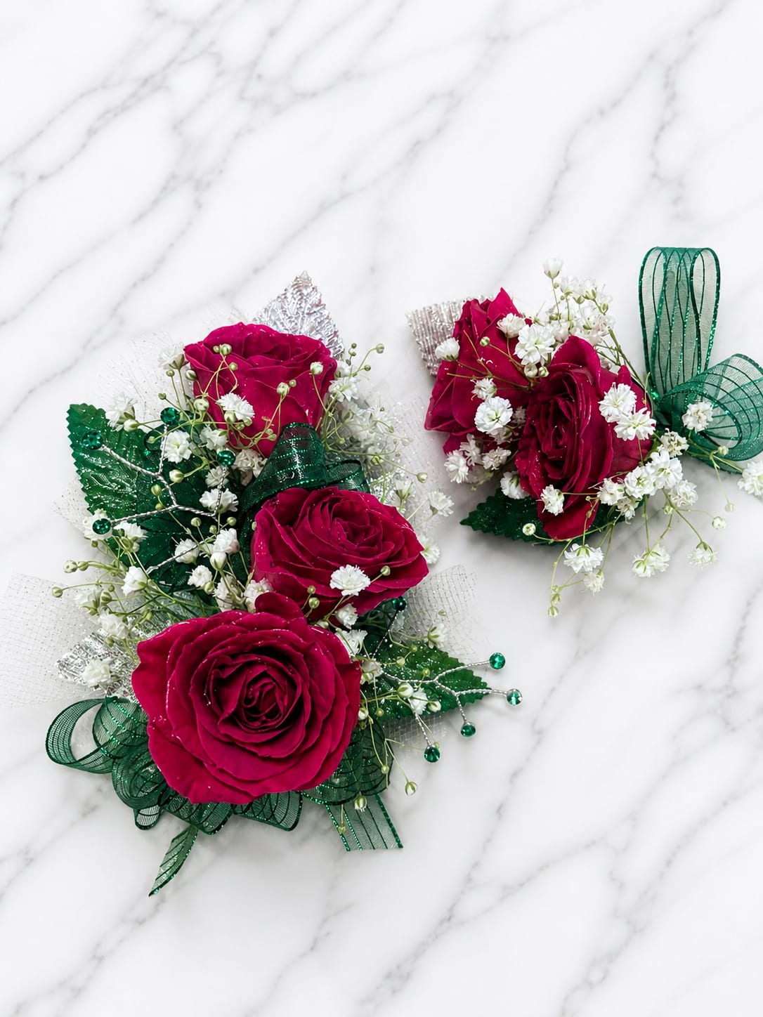 Emerald Envy Set - ️ MAGNETIC BOUTONNIERE WARNING: CONTAINS STRONG MAGNETS. DO NOT USE IF YOU HAVE A PACEMAKER, DEFIBRILLATOR, INSULIN PUMP, COCHLEAR IMPLANT, NEUROSTIMULATOR, OR OTHER IMPLANTED MEDICAL DEVICE. KEEP AWAY FROM ELECTRONICS, CREDIT CARDS, HOTEL KEY CARDS, AND CHILDREN.  Emerald Envy  Bold magenta roses and rich emerald accents create a striking wrist corsage and magnetic boutonniere set for prom, homecoming, dances, weddings, and formal events.  Standard includes a wrist corsage with 3 magenta roses and a matching magnetic boutonniere with 2 roses. Deluxe includes 4 roses in the corsage. Premium includes 5 roses in the corsage. All boutonnieres include 2 roses.  Each corsage and boutonniere is individually designed. Ribbon, filler flowers, bracelets, and decorative accents may vary based on availability. While individual details may differ, the overall color palette, flower count, style, and appearance of the Emerald Envy collection will be maintained.