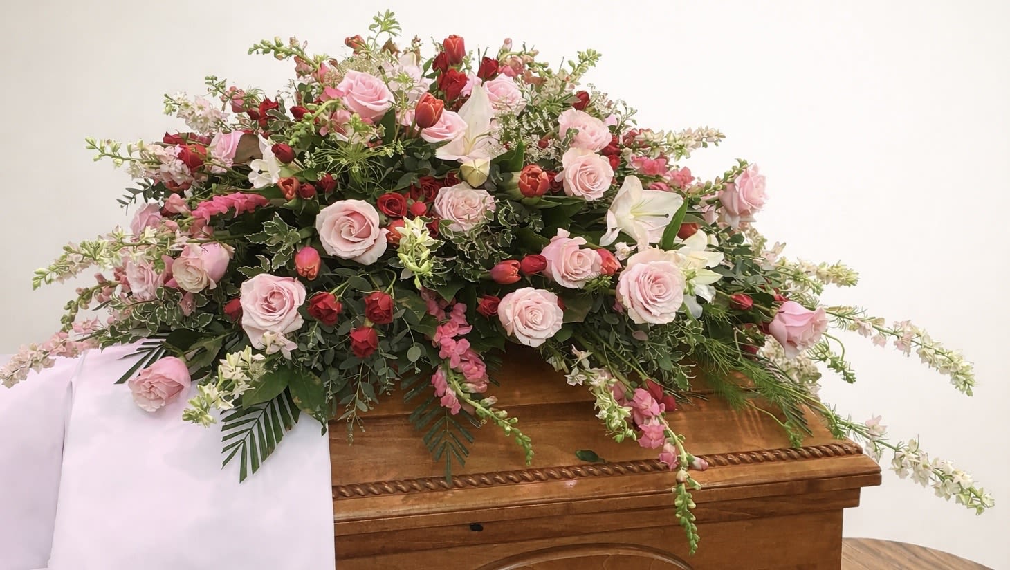 Always Beloved - Always Beloved is a romantic red and pink casket spray designed to make a powerful and lasting statement of love. Lush roses and complementary blooms are layered to create depth, movement, and presence, forming a tribute that feels both full and deeply personal.  The rich palette of reds and soft pinks symbolizes devotion, remembrance, and enduring connection, offering a graceful yet unmistakable expression of love and honor. Designed to rest beautifully atop the casket, this piece creates a focal point that carries emotion without overwhelming the space.  This design was originally created for a family served through Todd Funeral Centre &amp; Crematory, 1600 S State Road 3, Rushville, IN 46173. Families may learn more about Todd Funeral Centre &amp; Crematory at www.toddfuneralcentre.com.  Customers can view additional examples of our custom casket sprays in the Casket Spray section of our website, including real photographs and videos of funeral tributes created by Aspen Tower Florist.  Thoughtfully arranged with balance and intention, Always Beloved is a meaningful choice for honoring a life, a relationship, and a love that remains.